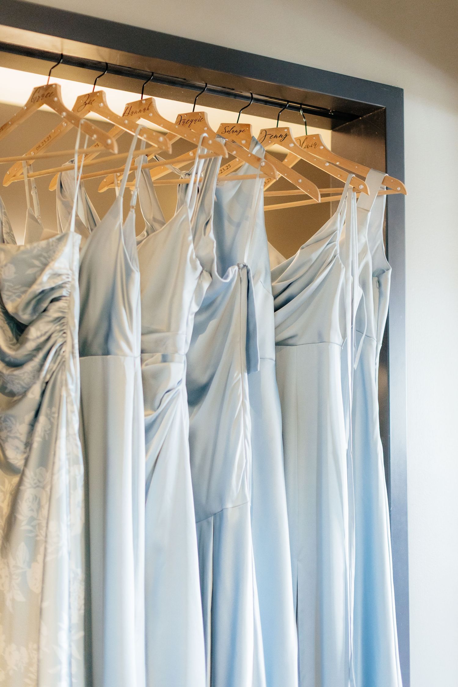 Row of light blue bridesmaid dresses hanging on wooden hangers in a closet.