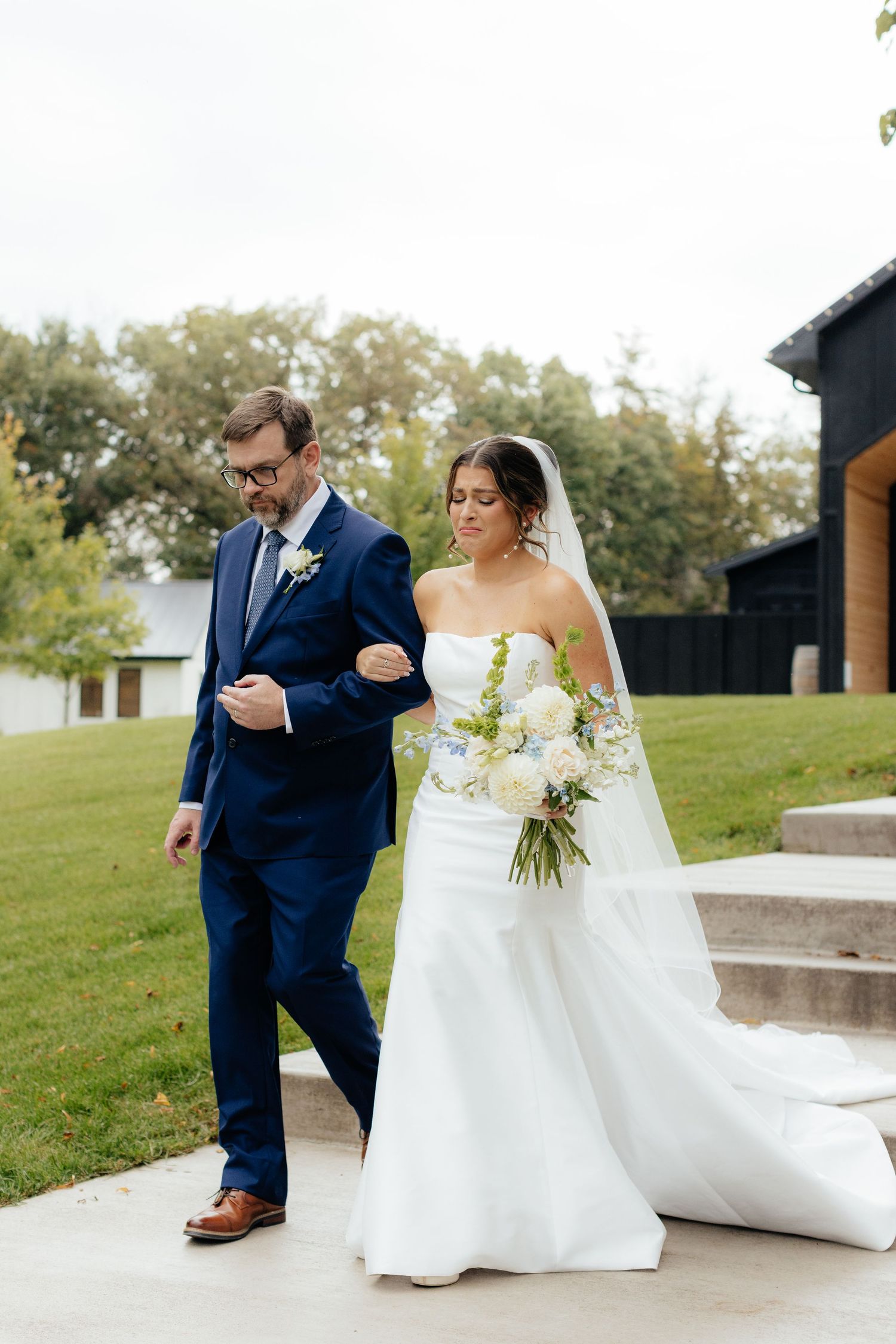 Wedding couple shares candid moments on concrete patio with grassy backdrop.