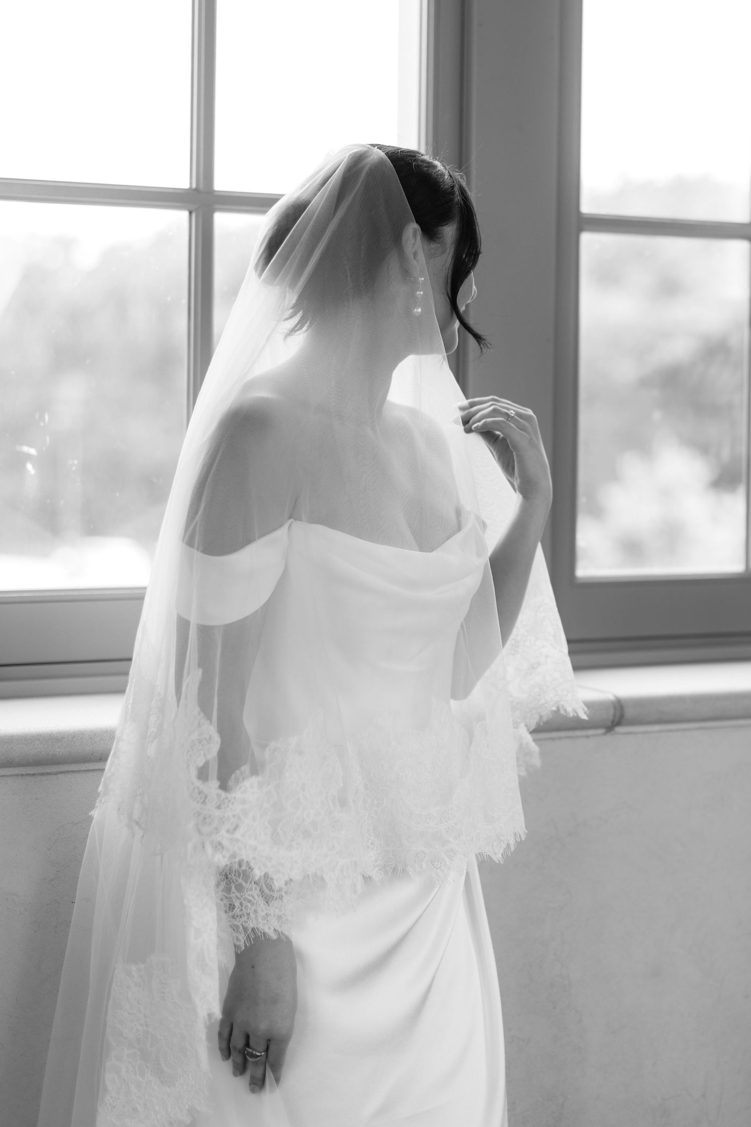 Artistic black and white photo series of a bride in her wedding gown by a window.