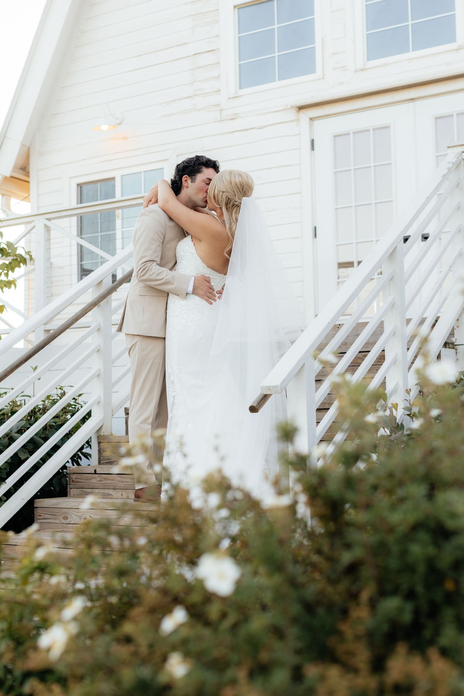 Romantic wedding couple embracing on white stairs outside a chapel during sunset.