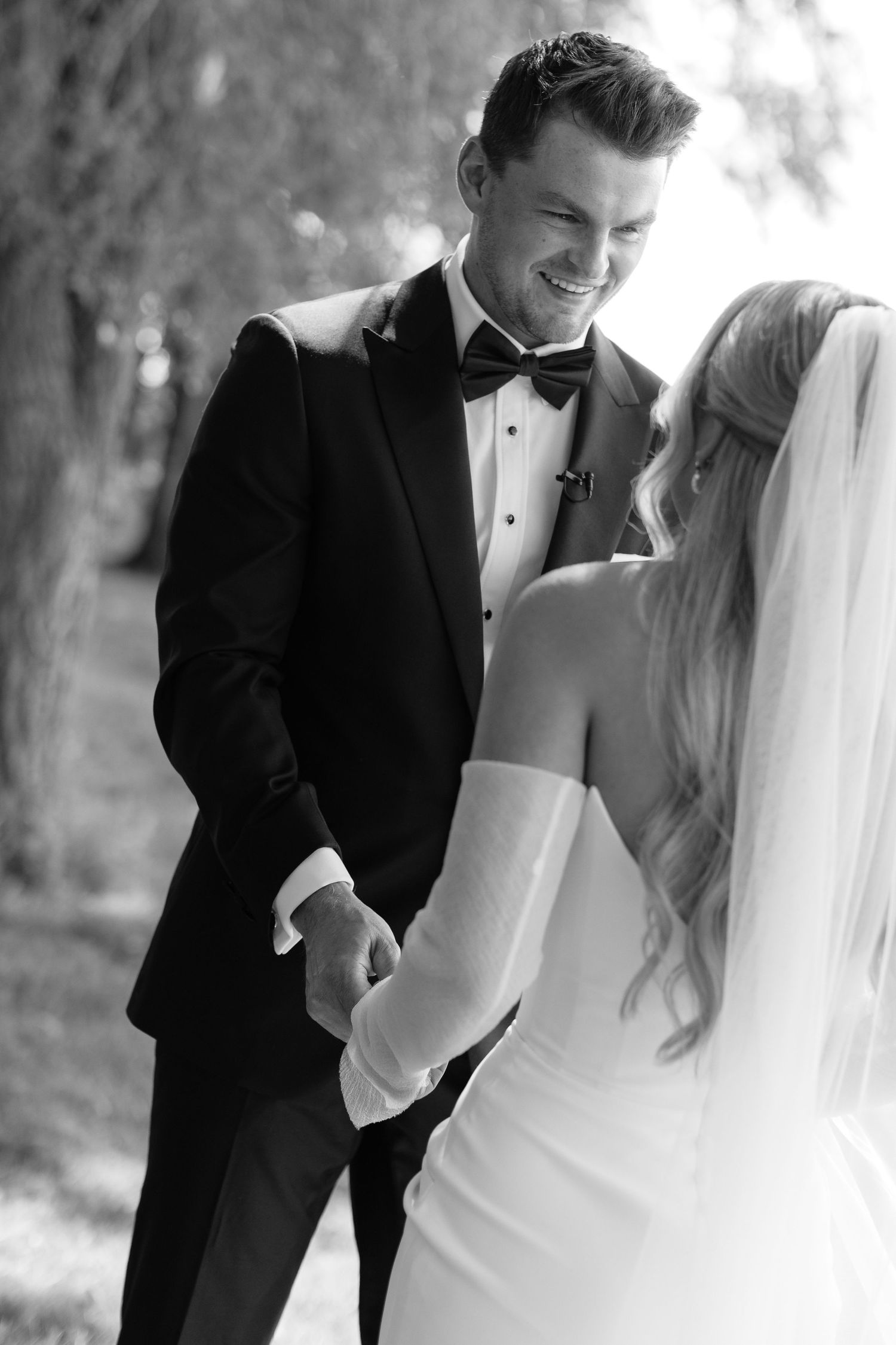 Black and white candid wedding photo showing joyful laughter between newlyweds.