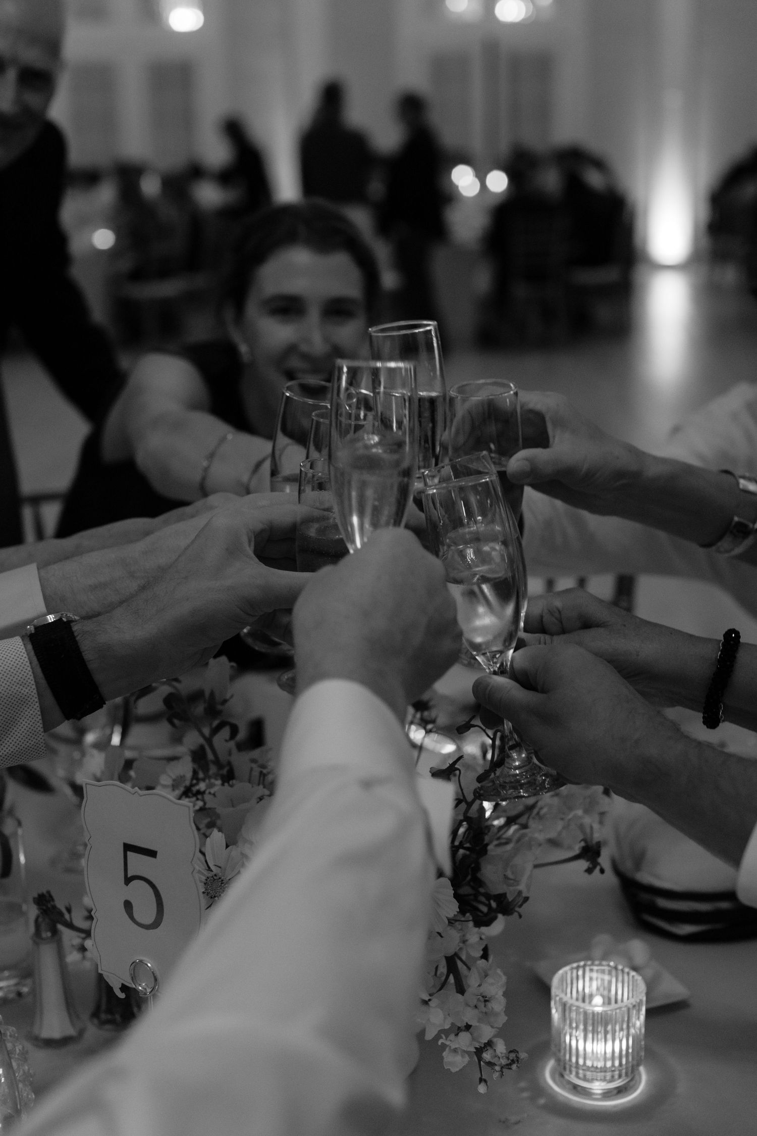 Wedding reception guests raise champagne glasses for a toast in dim lighting.