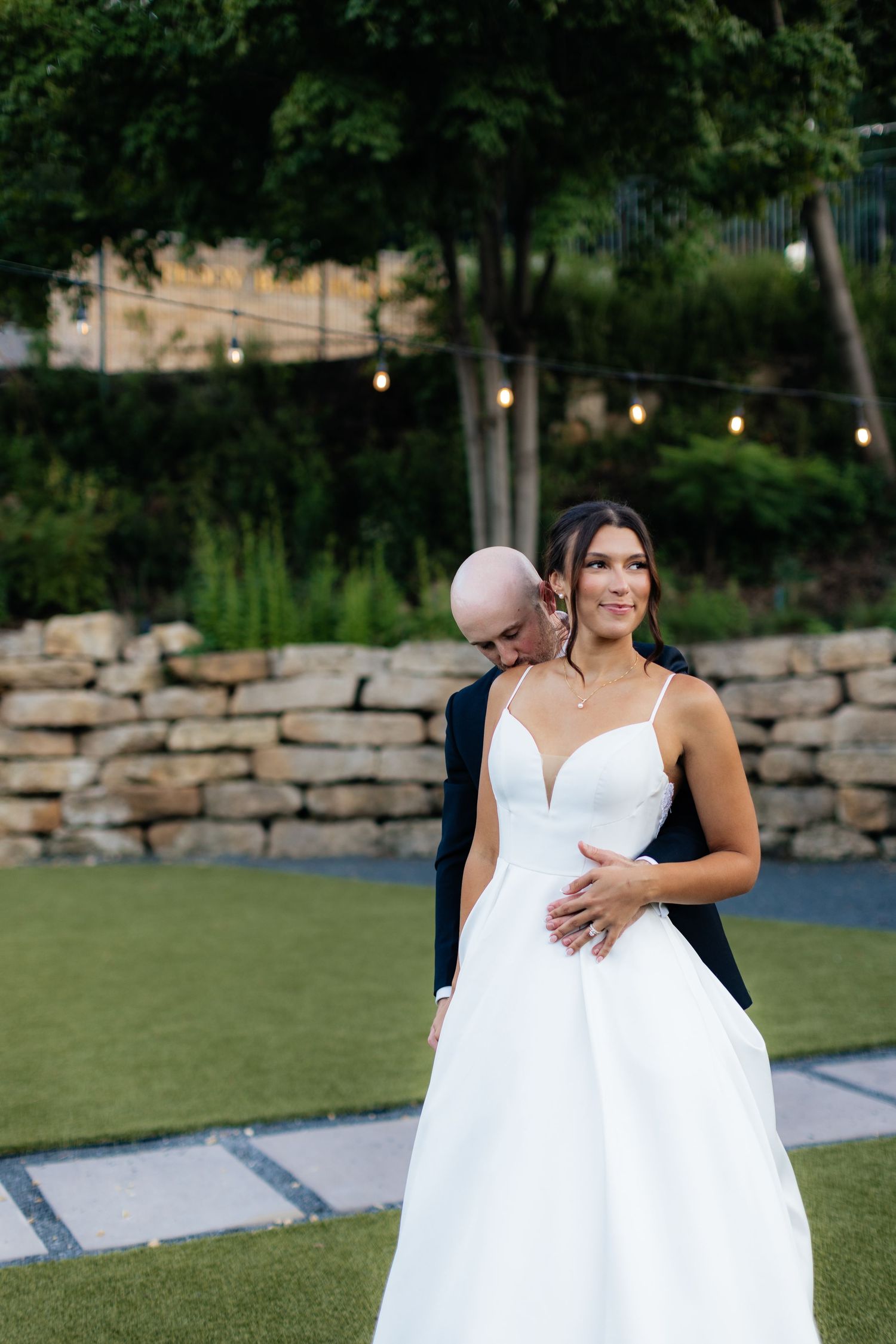 A couple dances together on a green lawn with decorative string lights overhead.