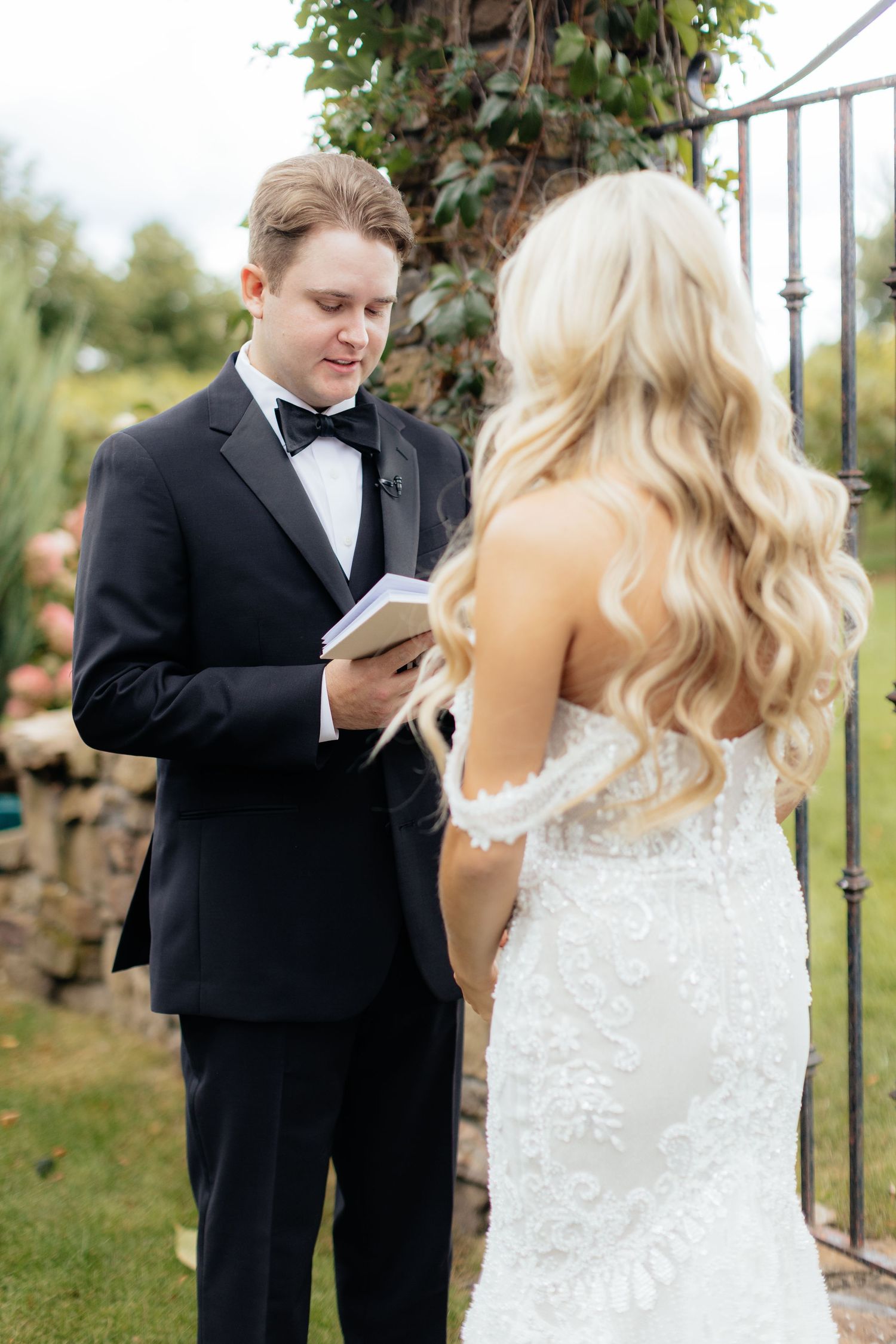 A couple exchanges vows during their outdoor wedding ceremony next to a stone wall.