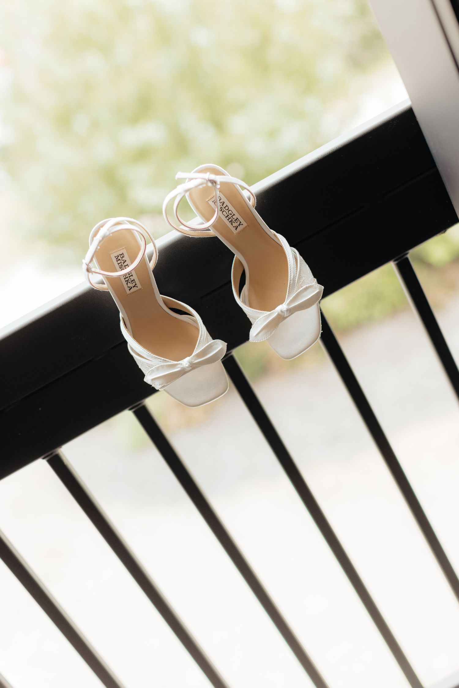 White strappy bridal sandals displayed on dark wooden railings.