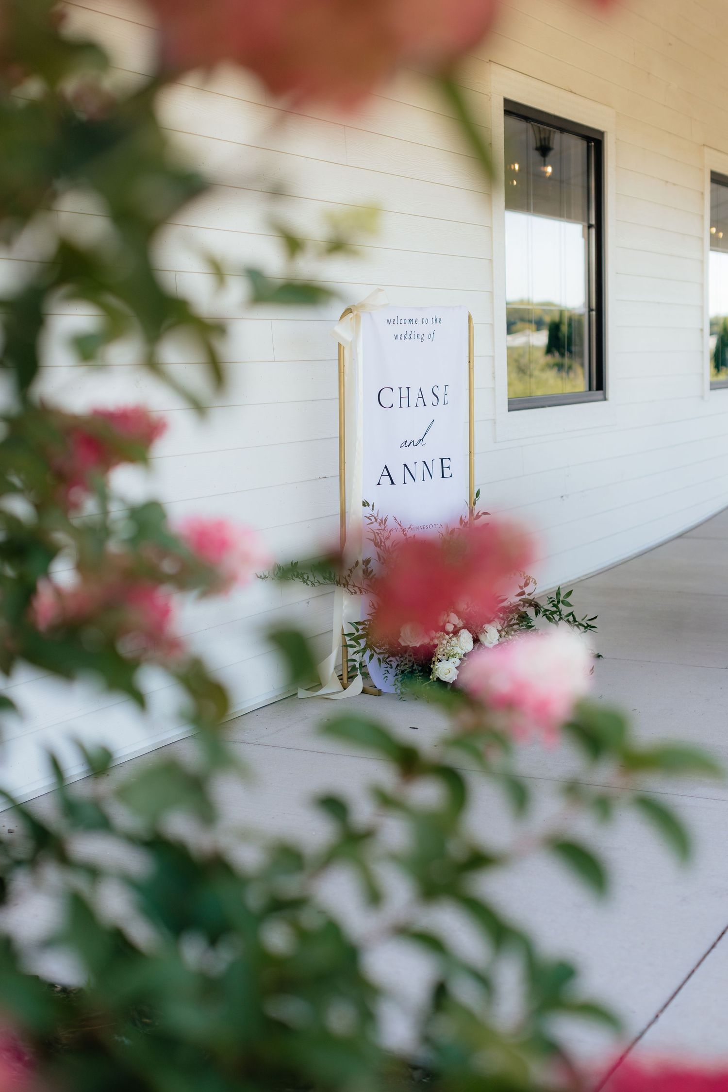 Wedding welcome sign with pink flowers in soft focus foreground.