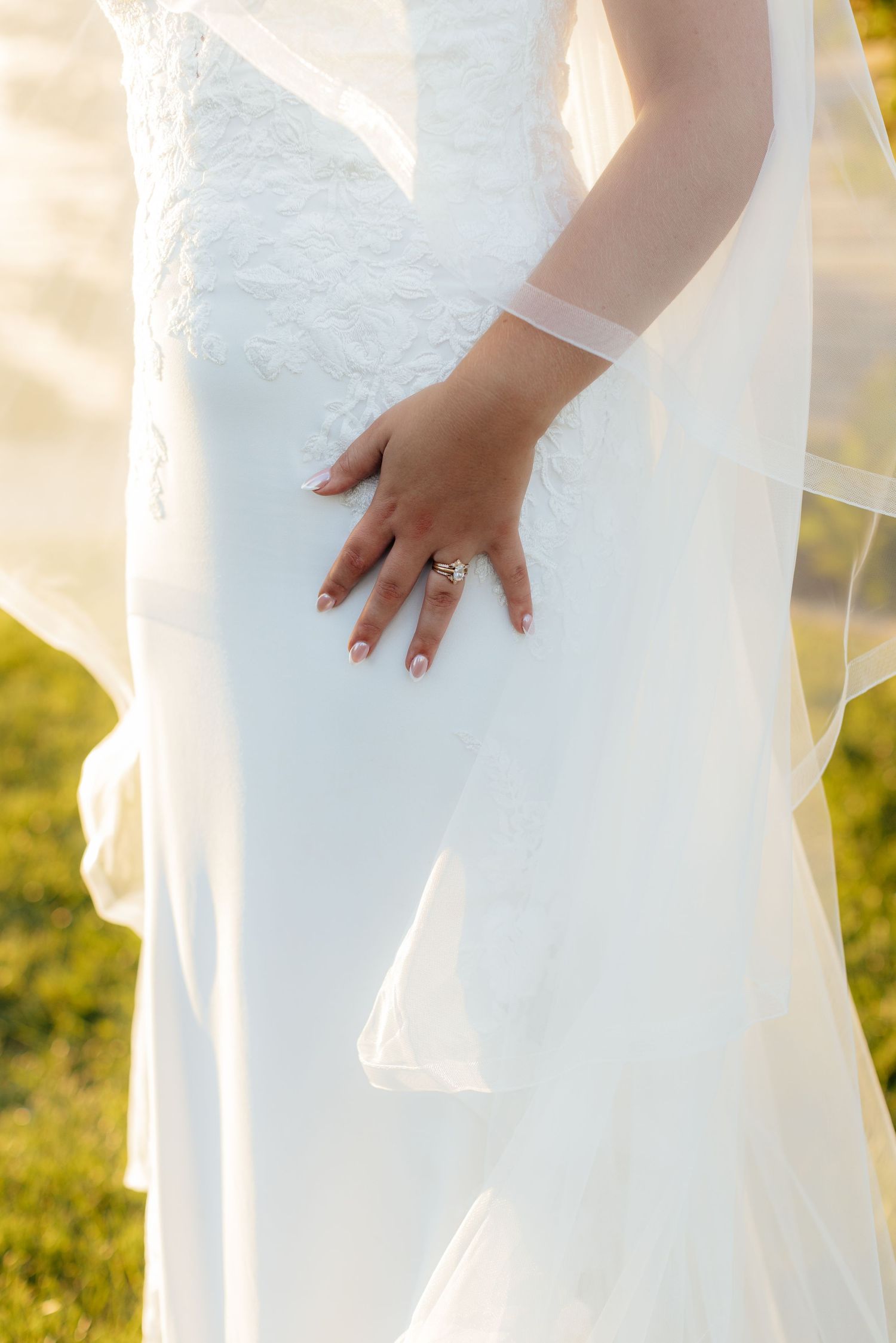 Close-up details of a white lace wedding dress against a sunny outdoor background.