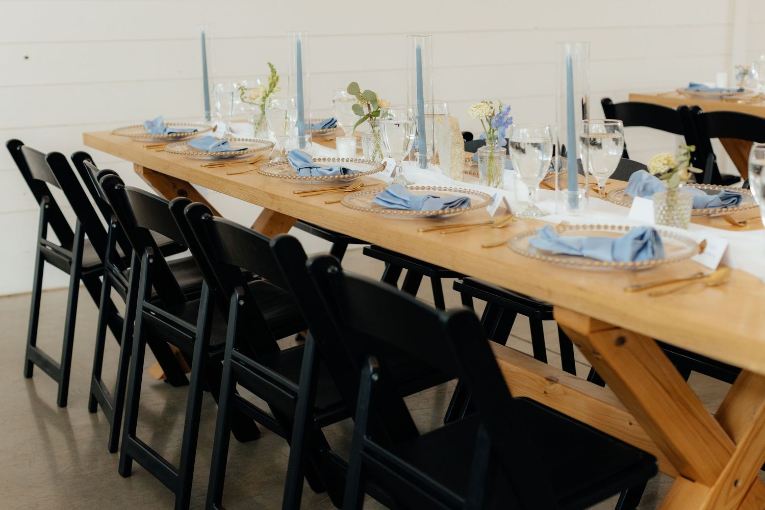 Rustic wedding reception table with light blue accents and black folding chairs.