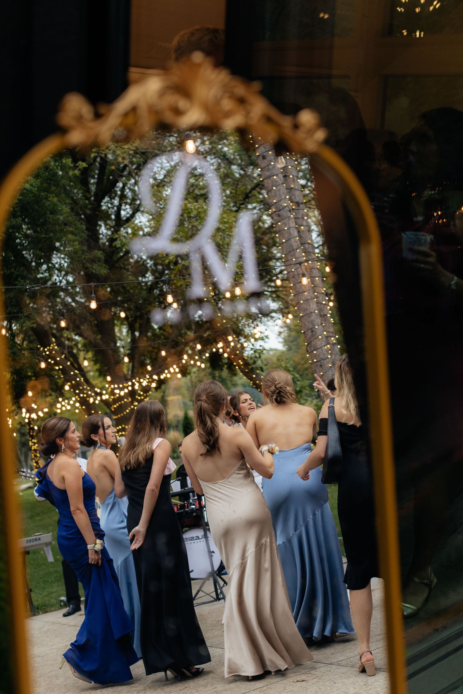 Elegant mirrored wedding monogram display with guests dancing in garden setting.