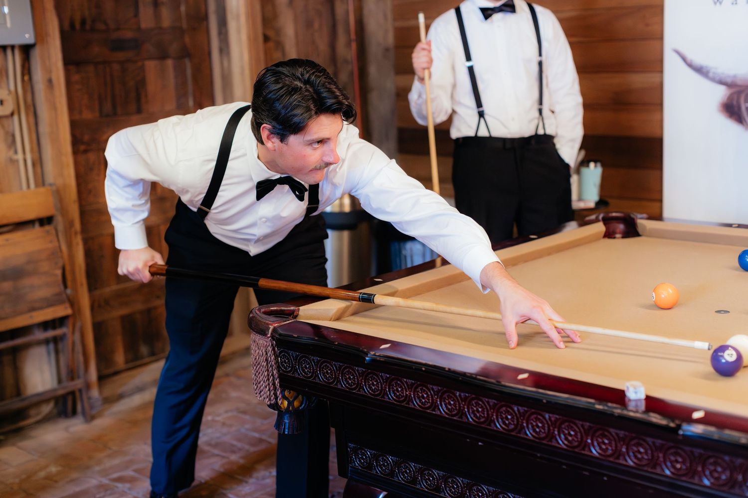 Men in formal attire playing pool at a rustic wooden venue.