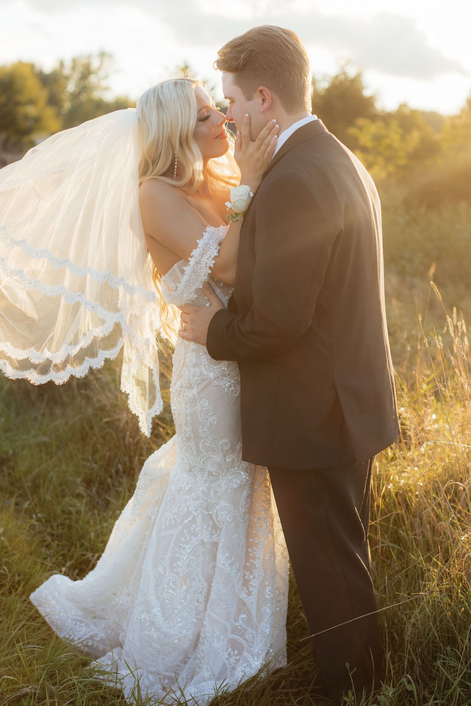 Golden hour wedding photos capture tender moments between bride and groom in a sunlit field.