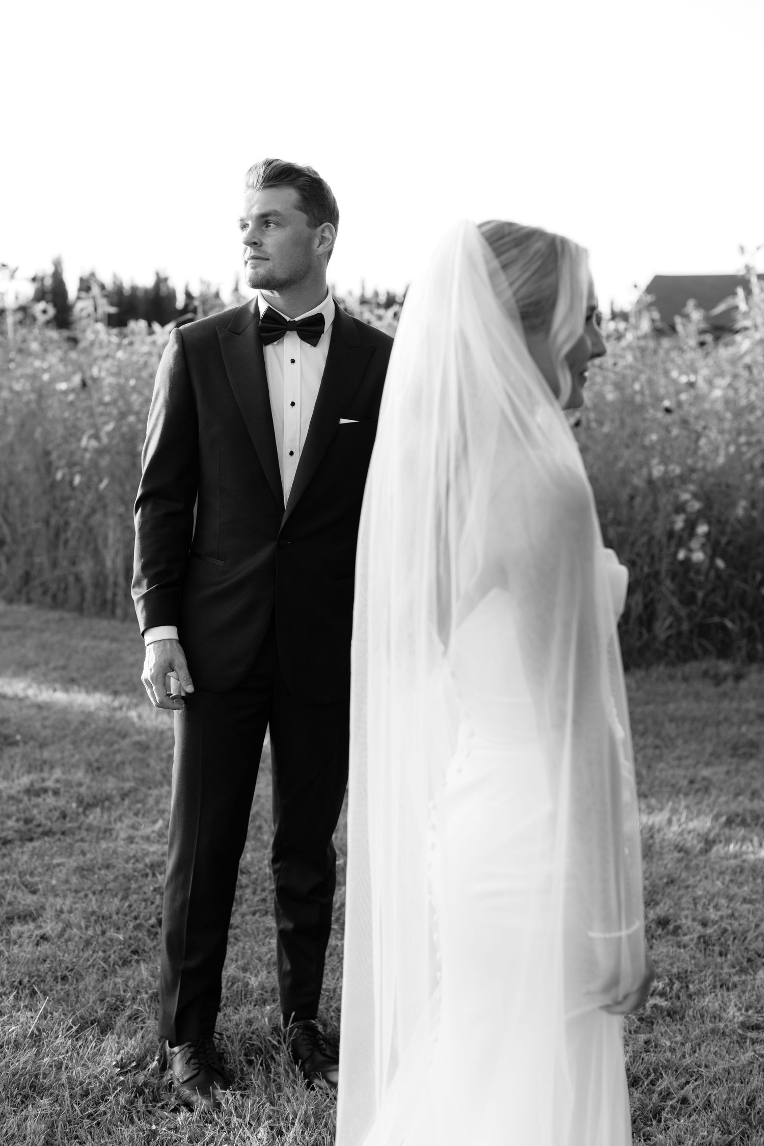 Black and white portrait of a wedding couple standing in a field during their special day.
