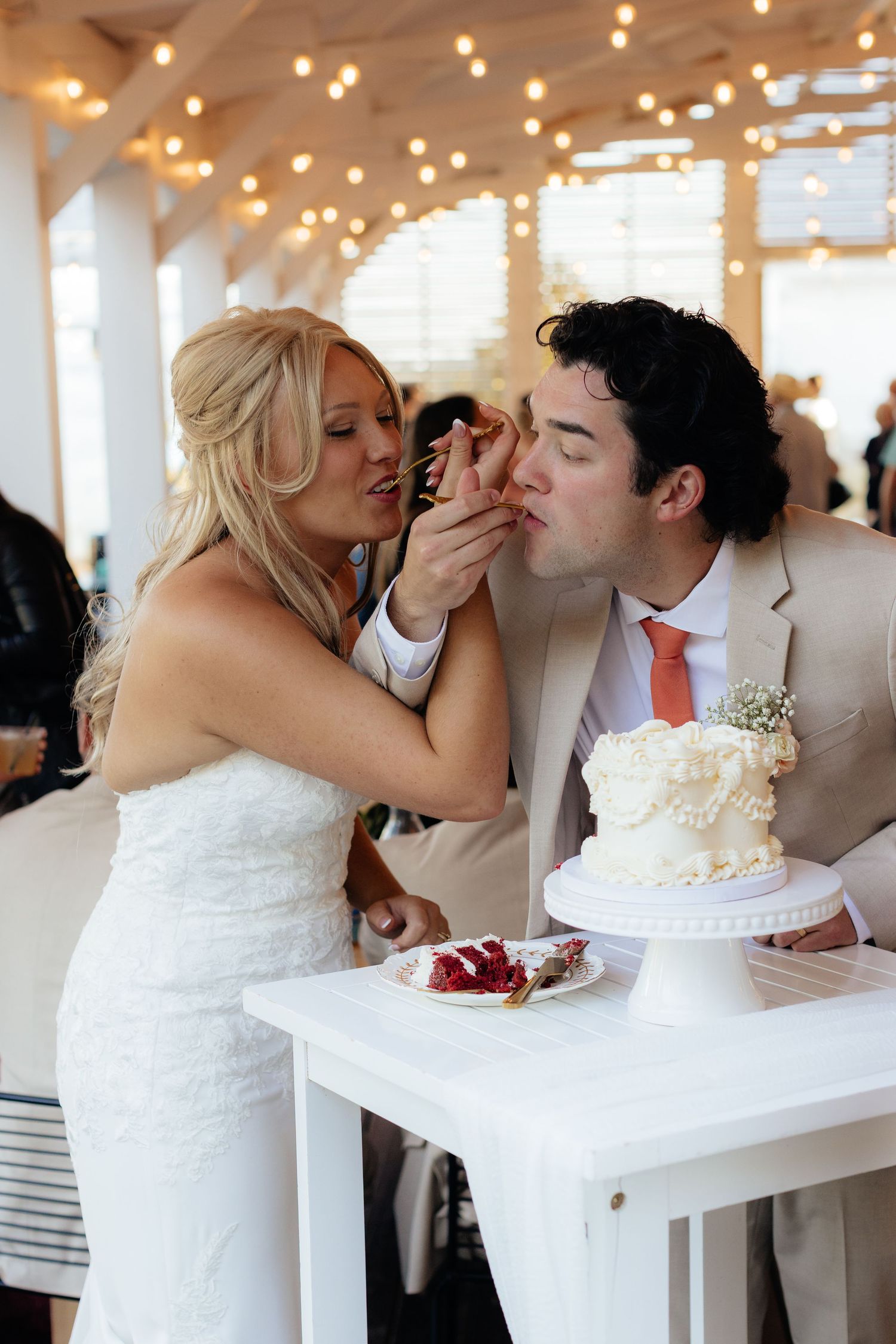 Wedding couple sharing cake during traditional cake cutting ceremony under string lights.