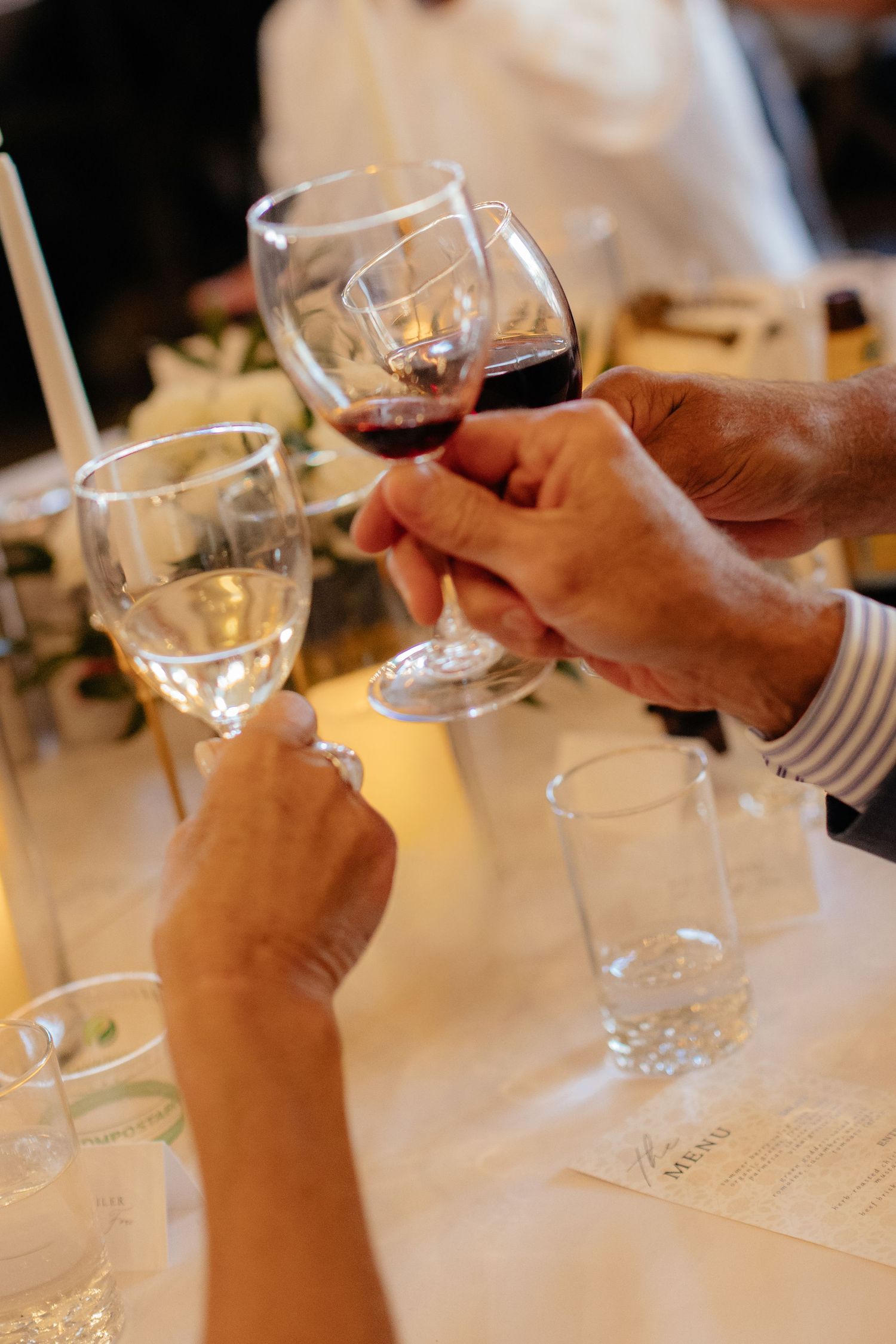Wedding guests toasting with red and white wine glasses over a white tablecloth.