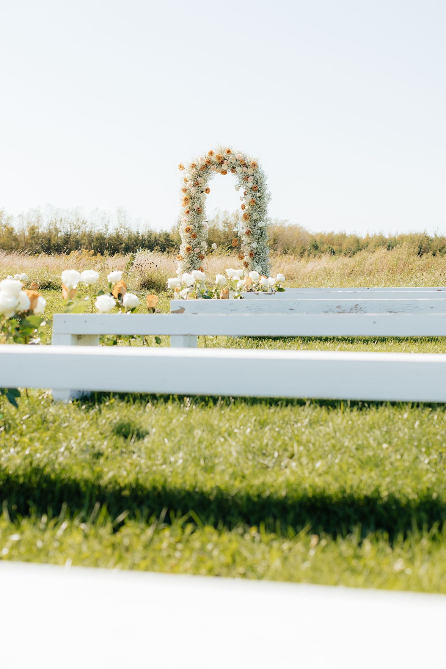 Floral wedding arch and white fencing in an outdoor ceremony setting.