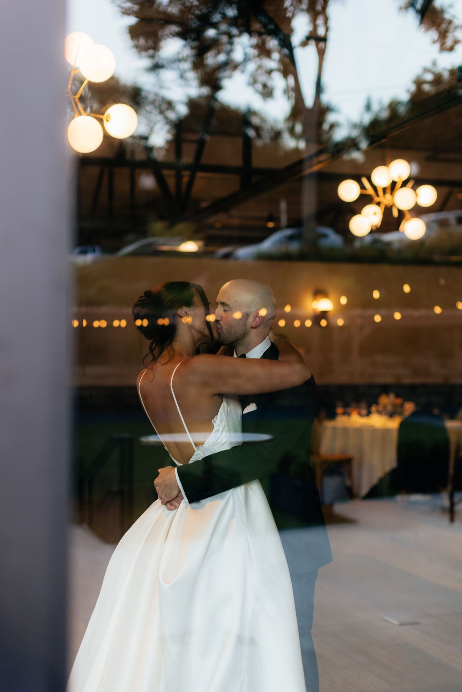A couple embraces during a dance at an outdoor evening event with twinkling lights.