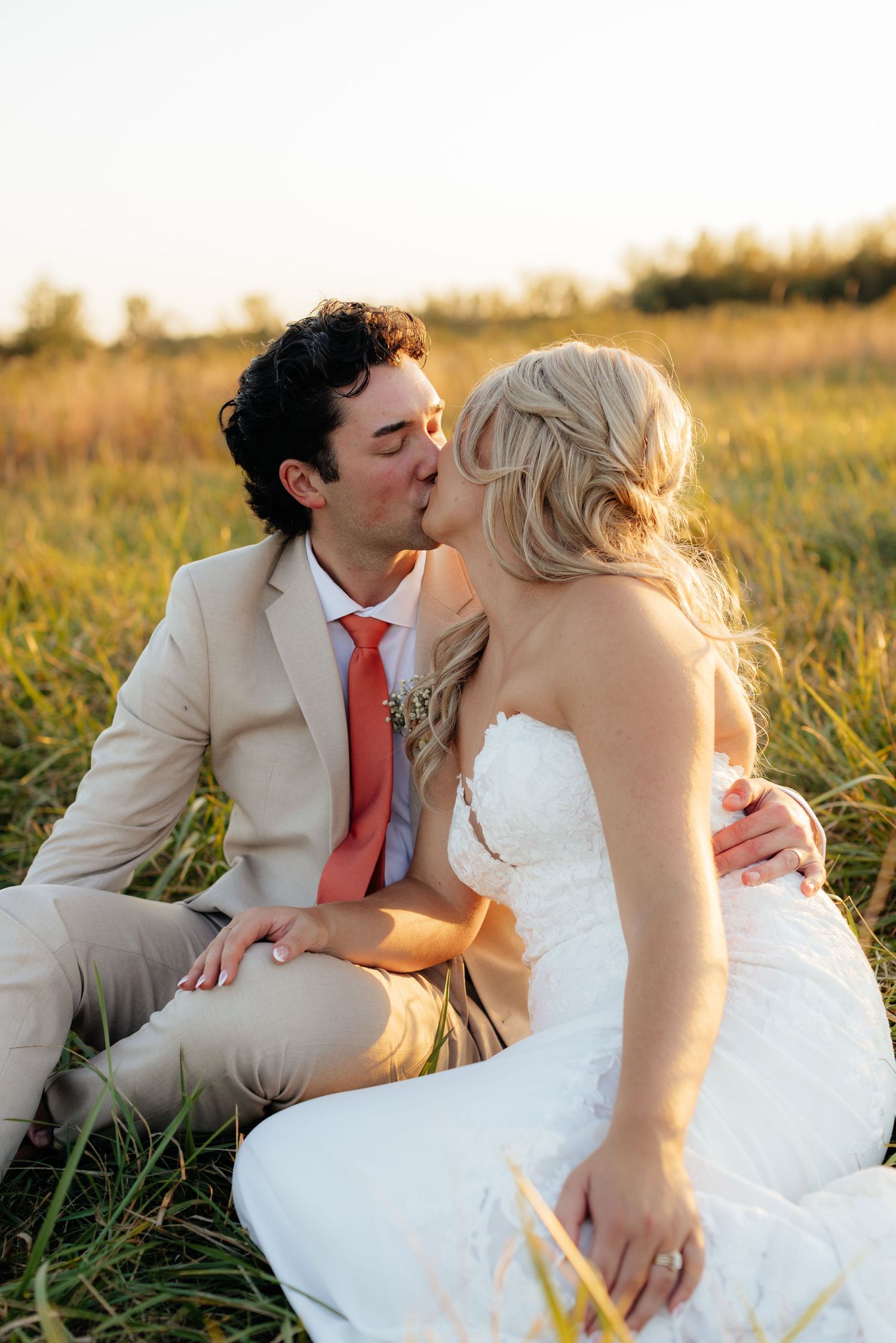 Newlyweds share intimate moments while sitting in a sunlit meadow.