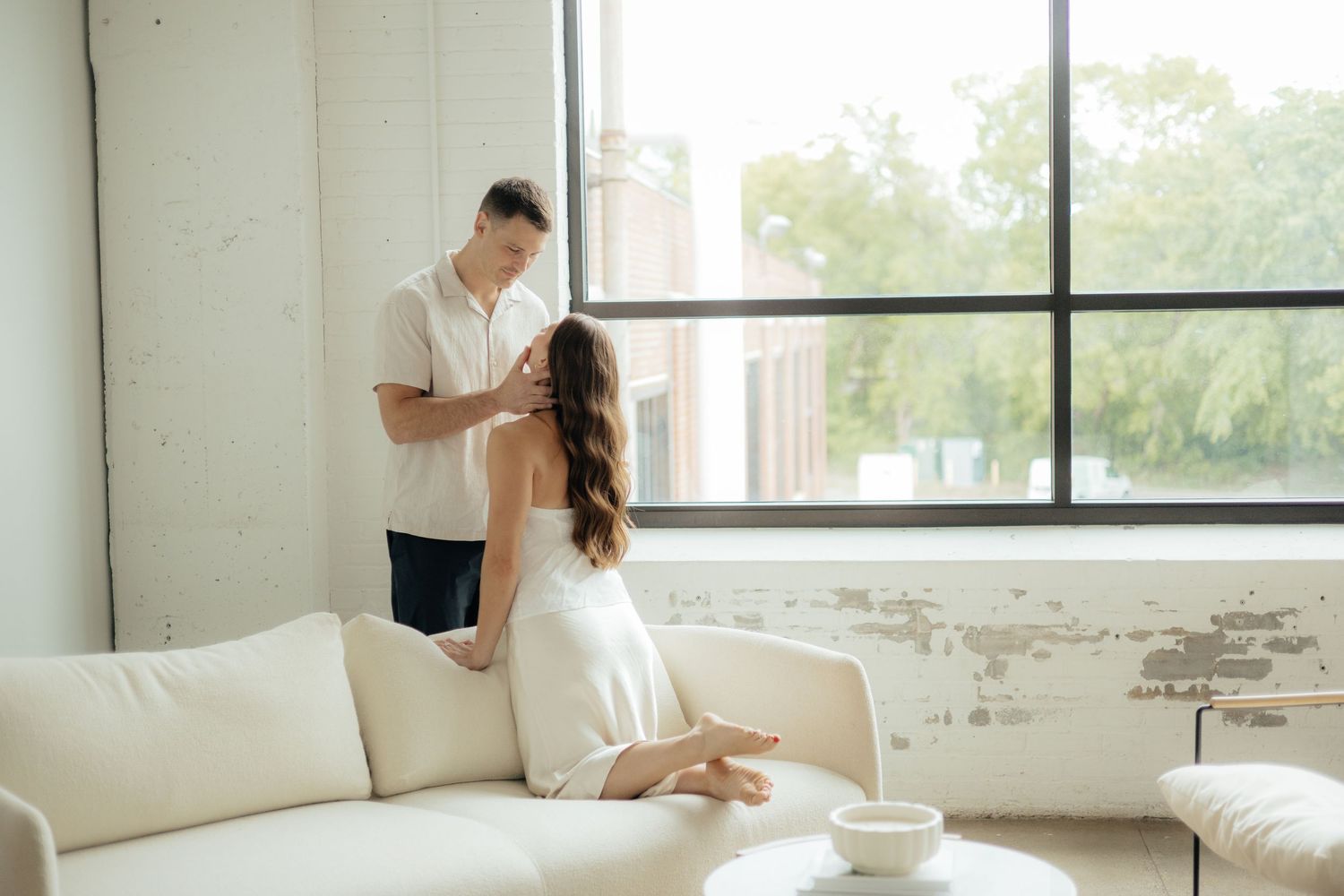 Couple relaxes together in bright minimalist white room with large windows.