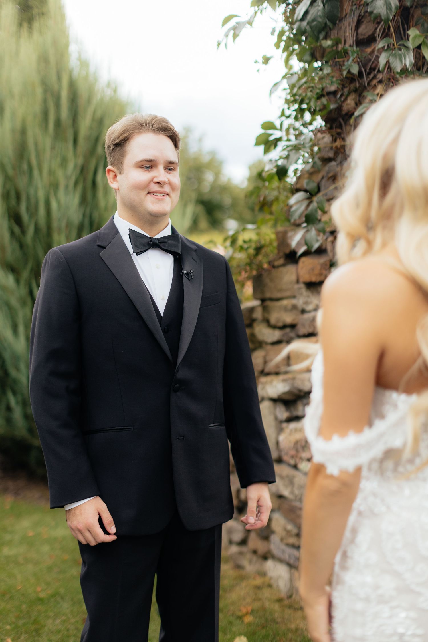 A groom in a black tuxedo shares a special moment during a first look at an outdoor wedding.
