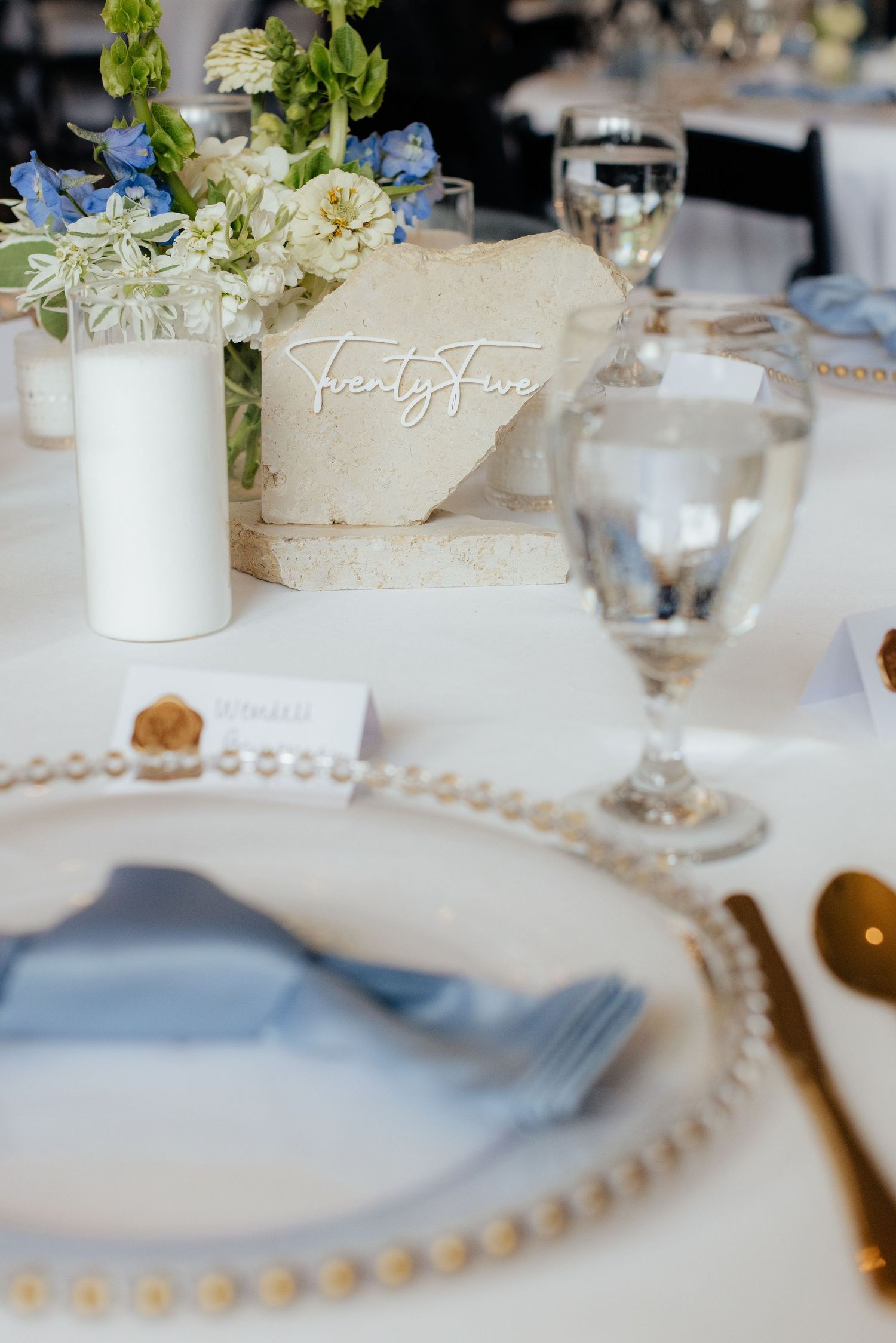 Elegant wedding table setting with blue and white floral centerpiece and beaded charger plates.