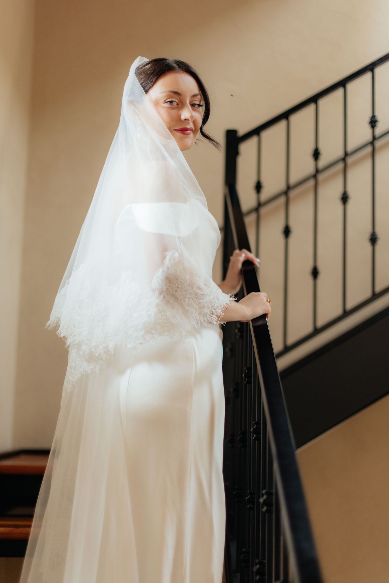 Bride in flowing white dress poses elegantly on a staircase with iron railings.