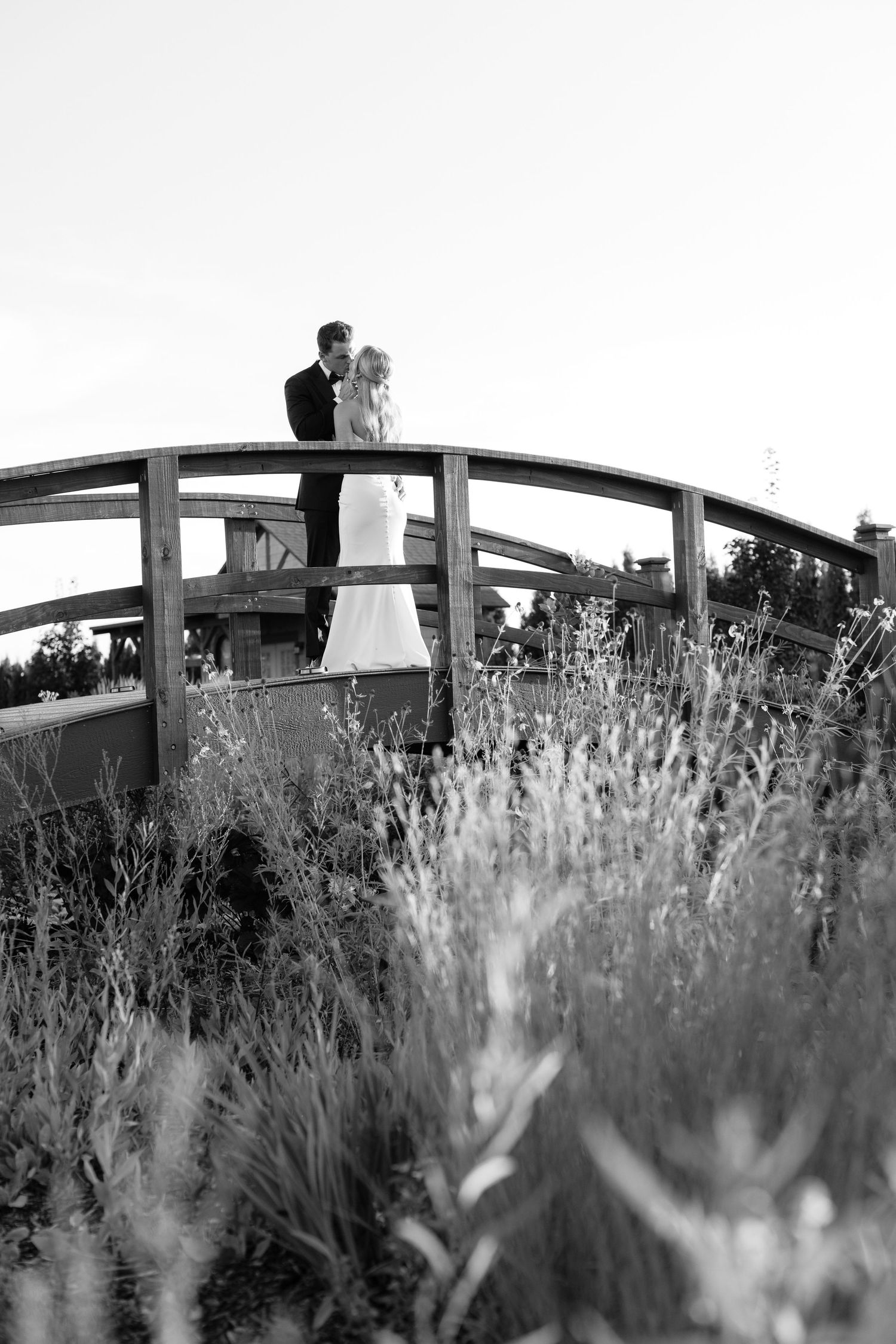 Black and white artistic photo of a couple on a bridge with wildflowers in foreground.