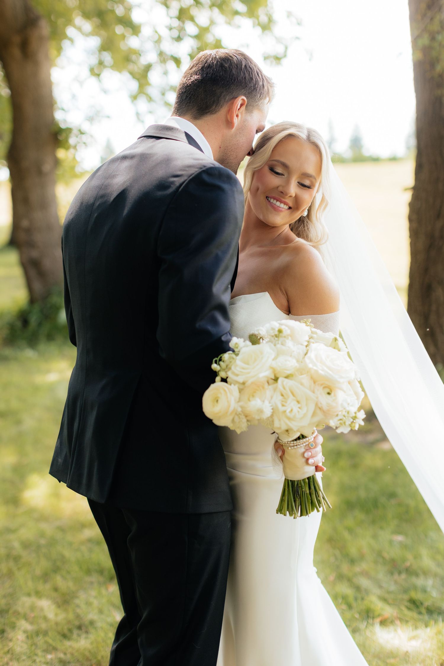 Tender moment between newlyweds with white bouquet in outdoor setting.