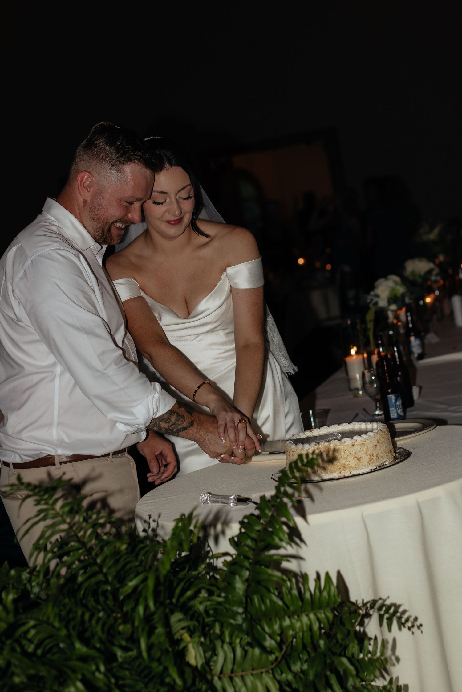 Couple cuts their wedding cake together at an evening reception with candlelight.