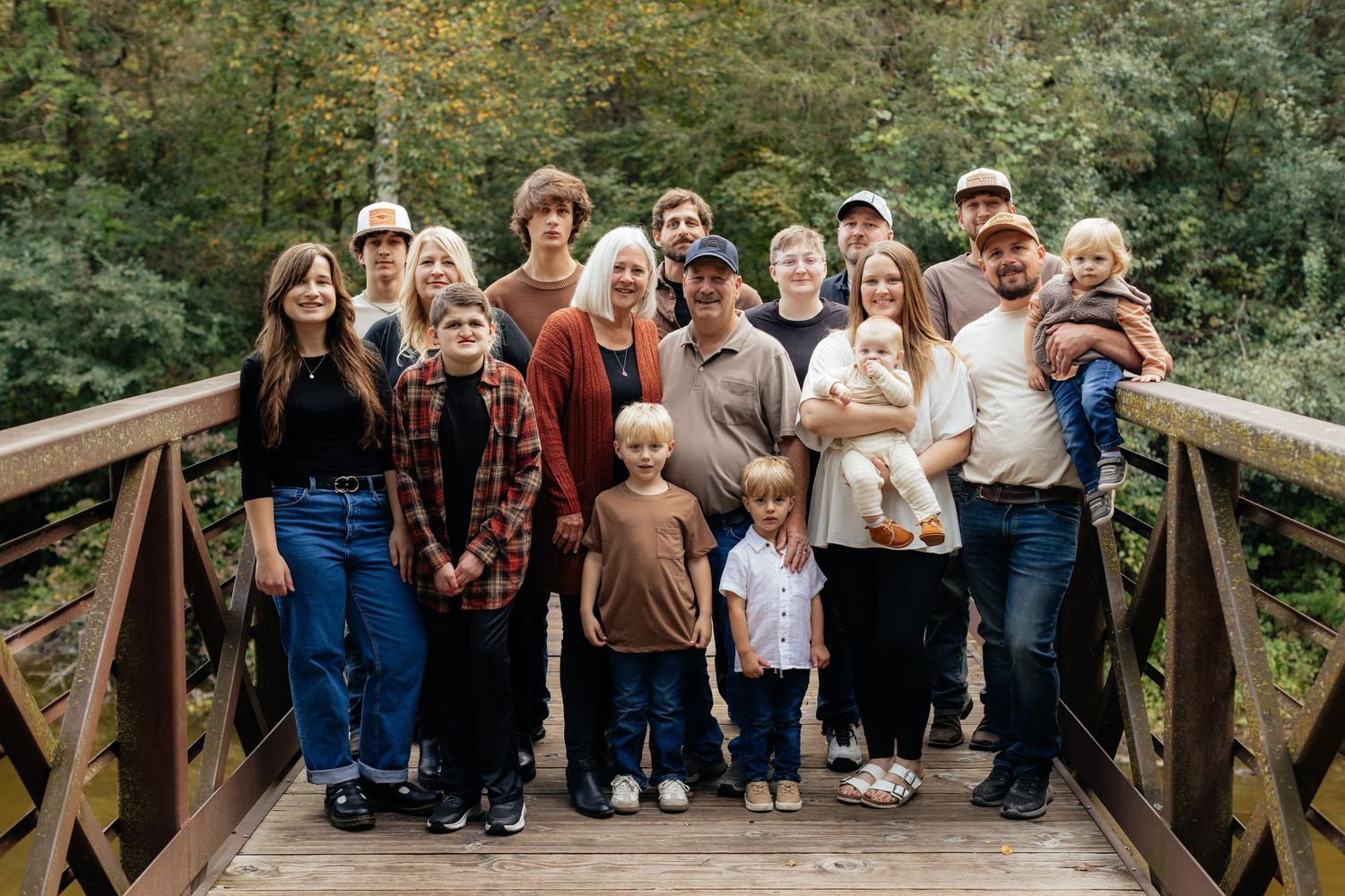 Large family group poses together on a wooden bridge in an outdoor nature setting.