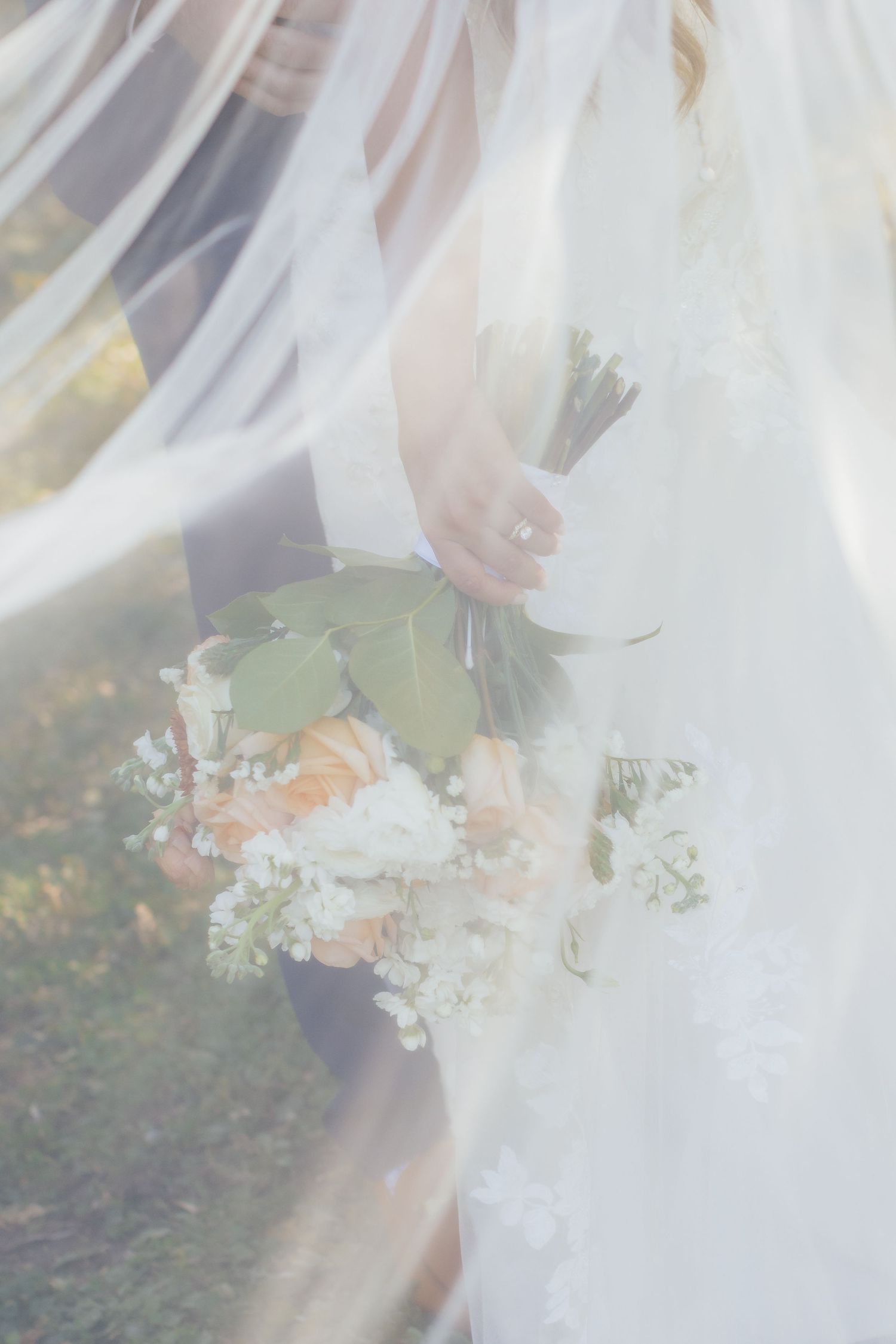 Ethereal close-up of bridal bouquet through flowing white veil.