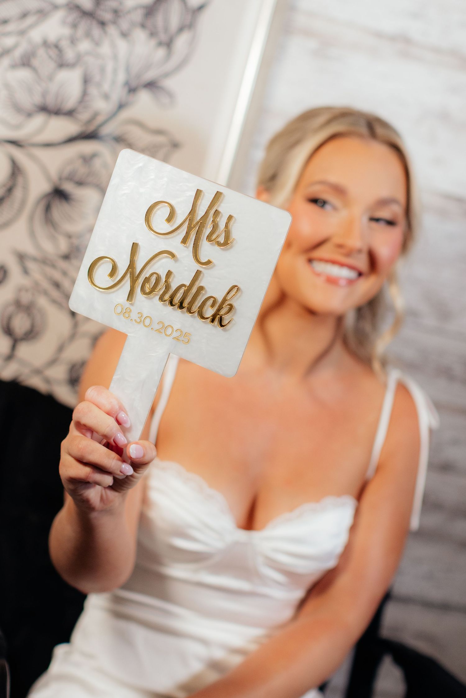 A decorative wedding sign reading 'Mrs Nordick' held up against a floral background.