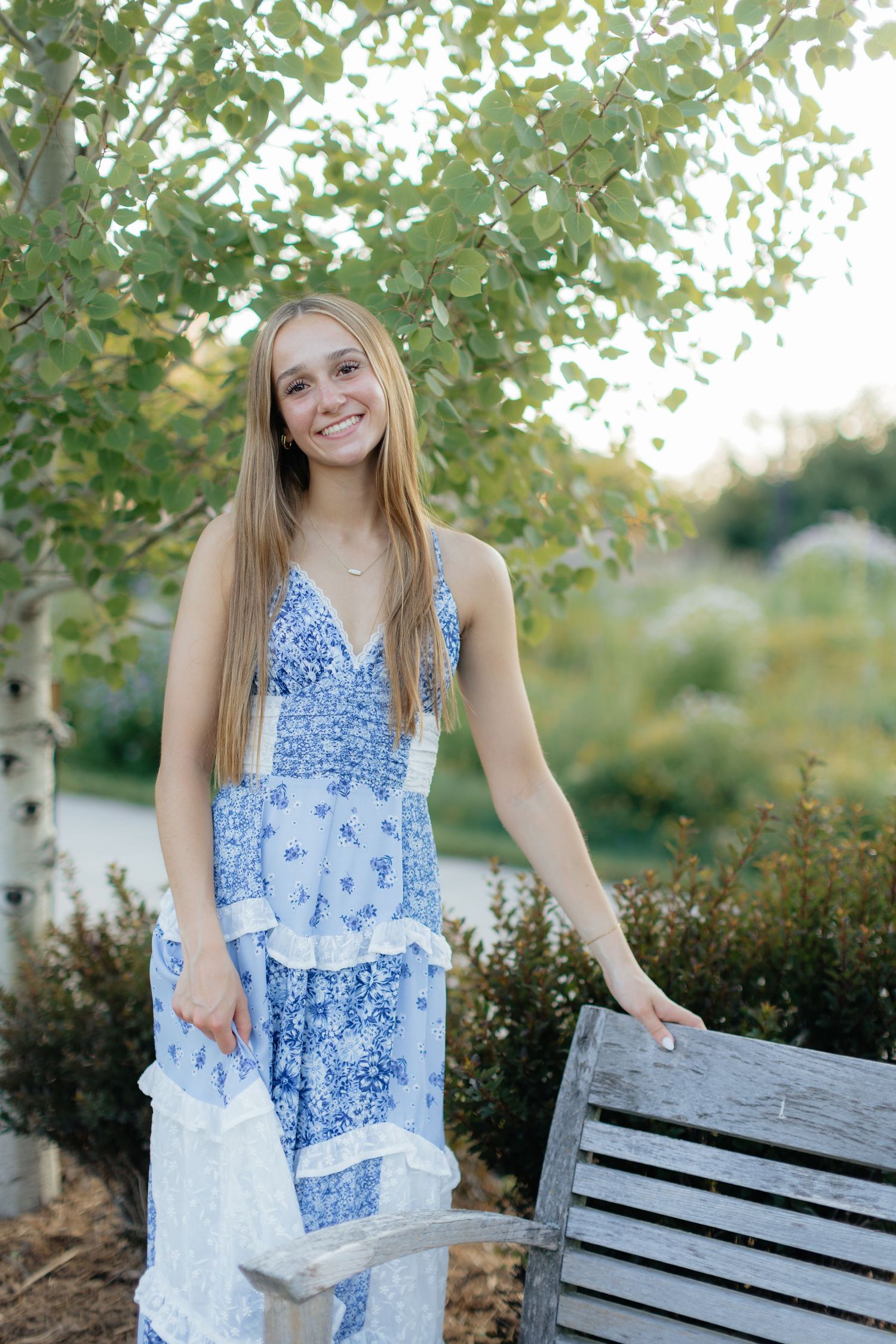 A blue and white patterned maxi dress is showcased in a garden setting near a wooden bench.