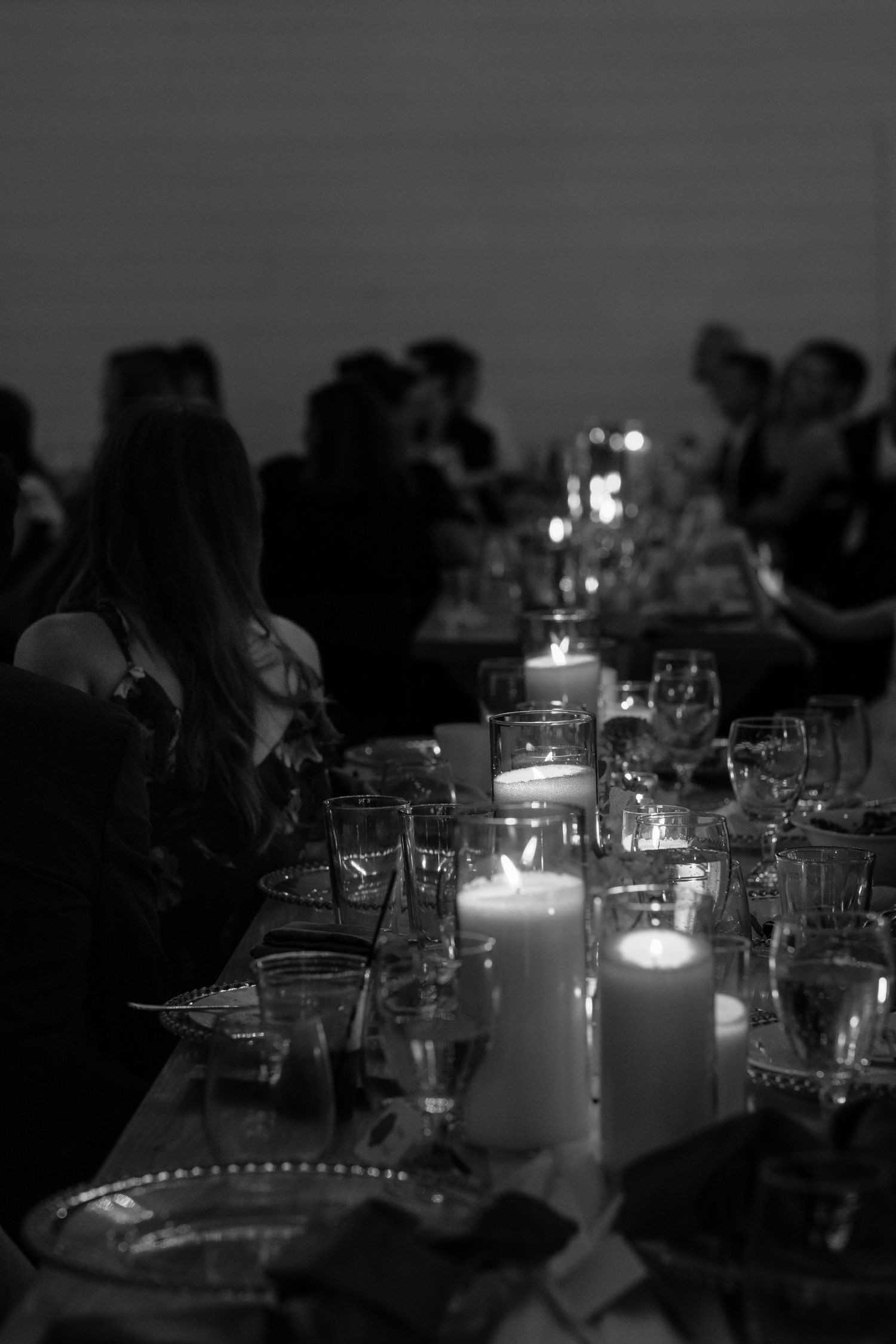Candlelit wedding reception table setting with glowing centerpieces in dark ambient lighting.