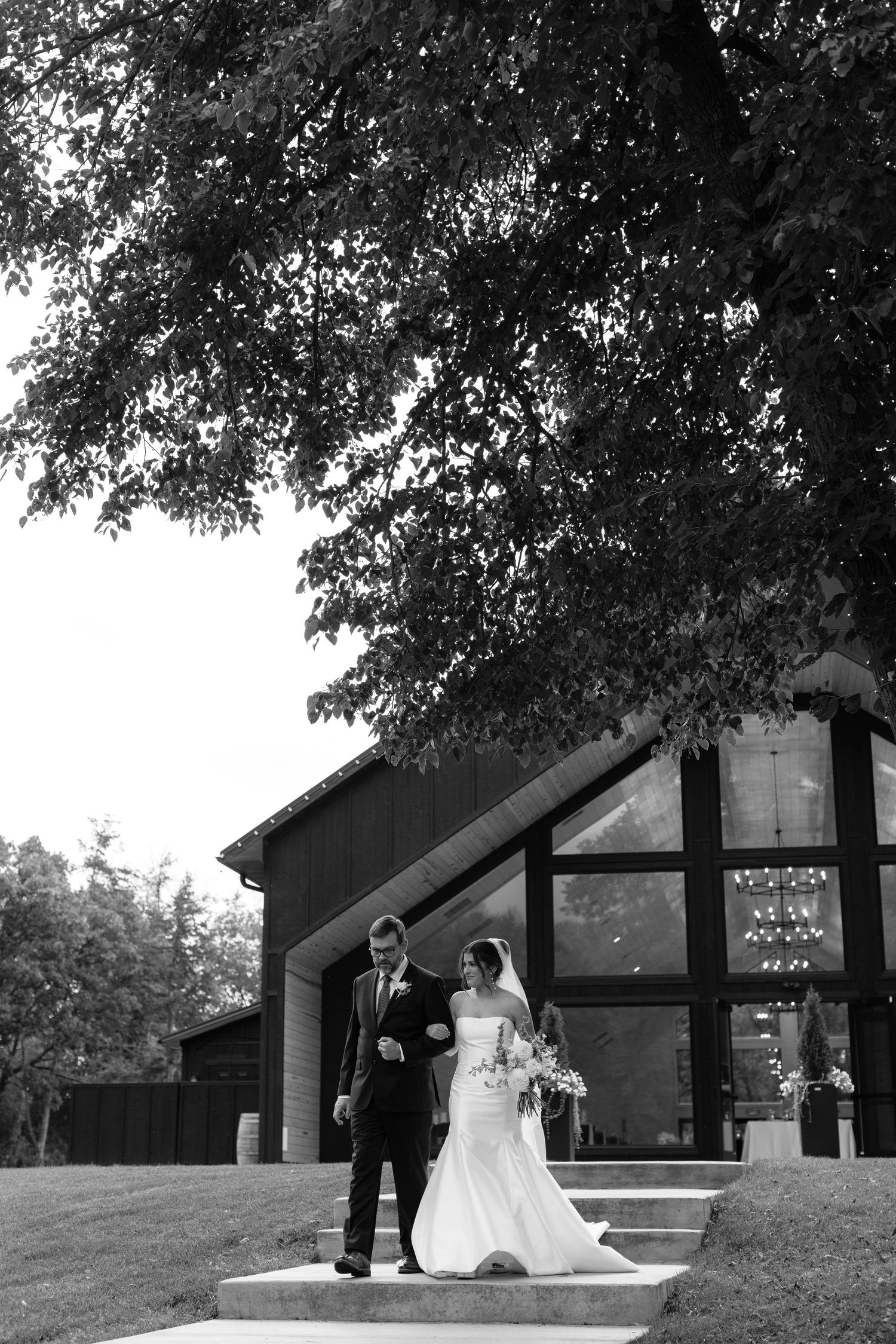 Black and white photo of wedding couple walking outside modern chapel building.