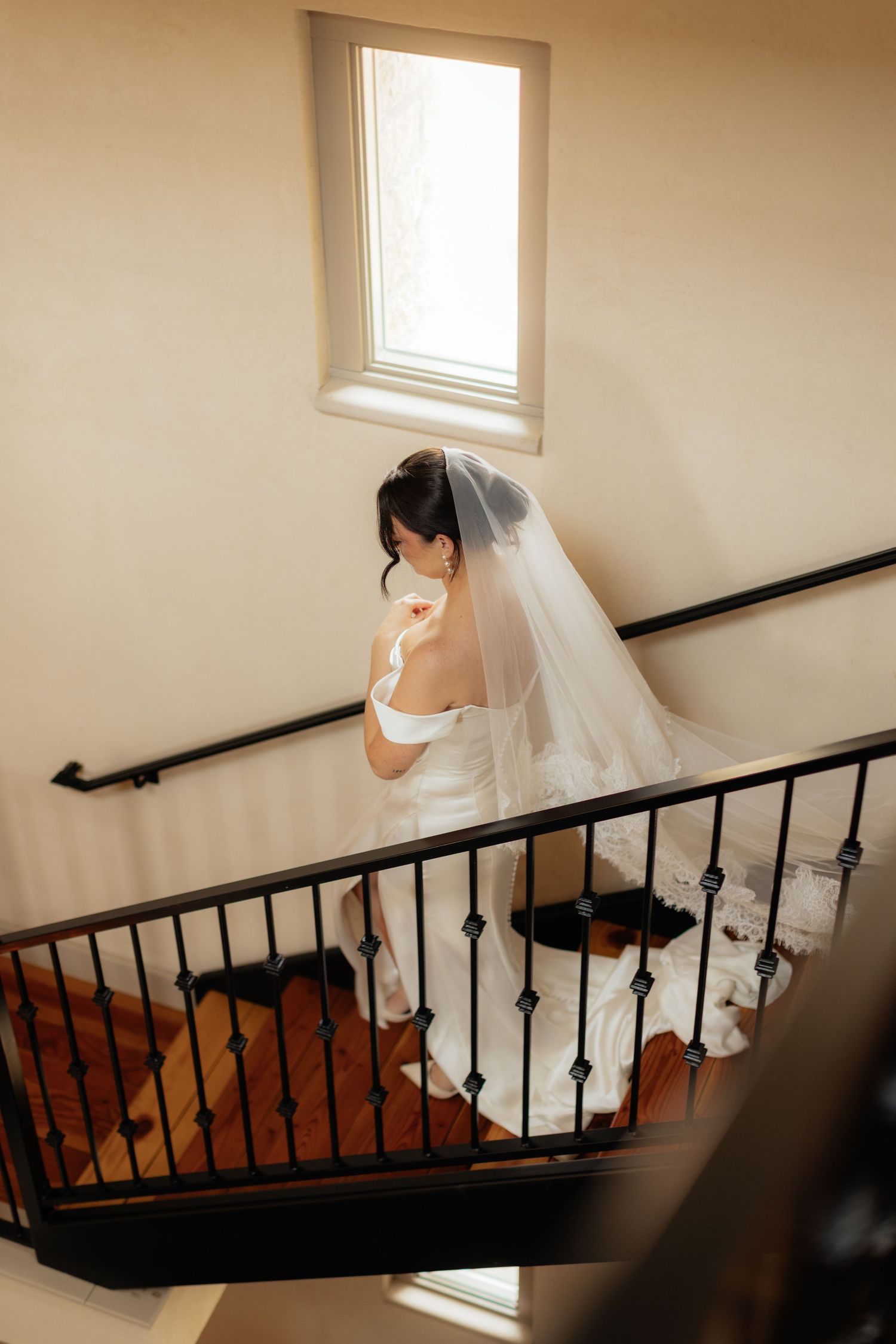 Bride in white dress ascending a staircase with decorative iron railings.