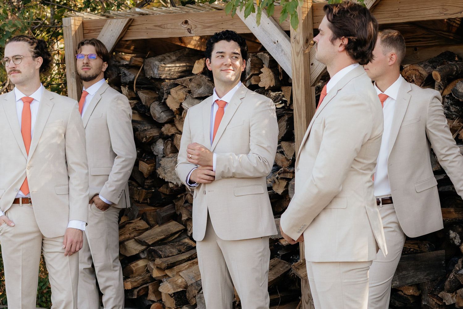 Groomsmen in tan suits with coral ties share laughs during outdoor wedding photos.