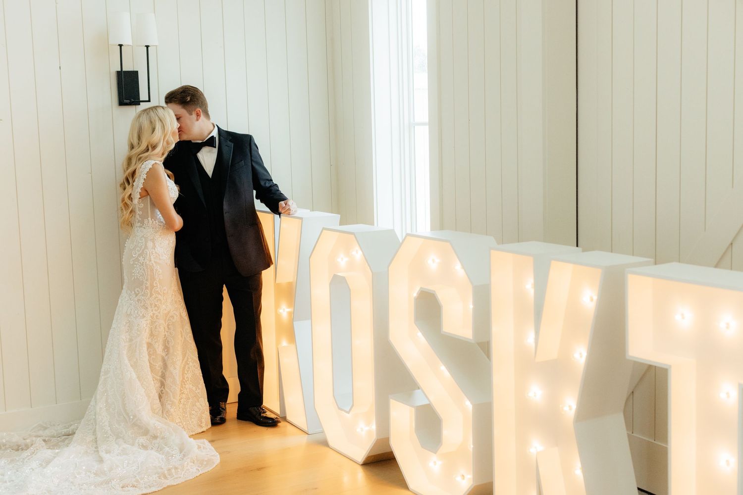 Wedding portraits in modern white room with illuminated marquee letters.