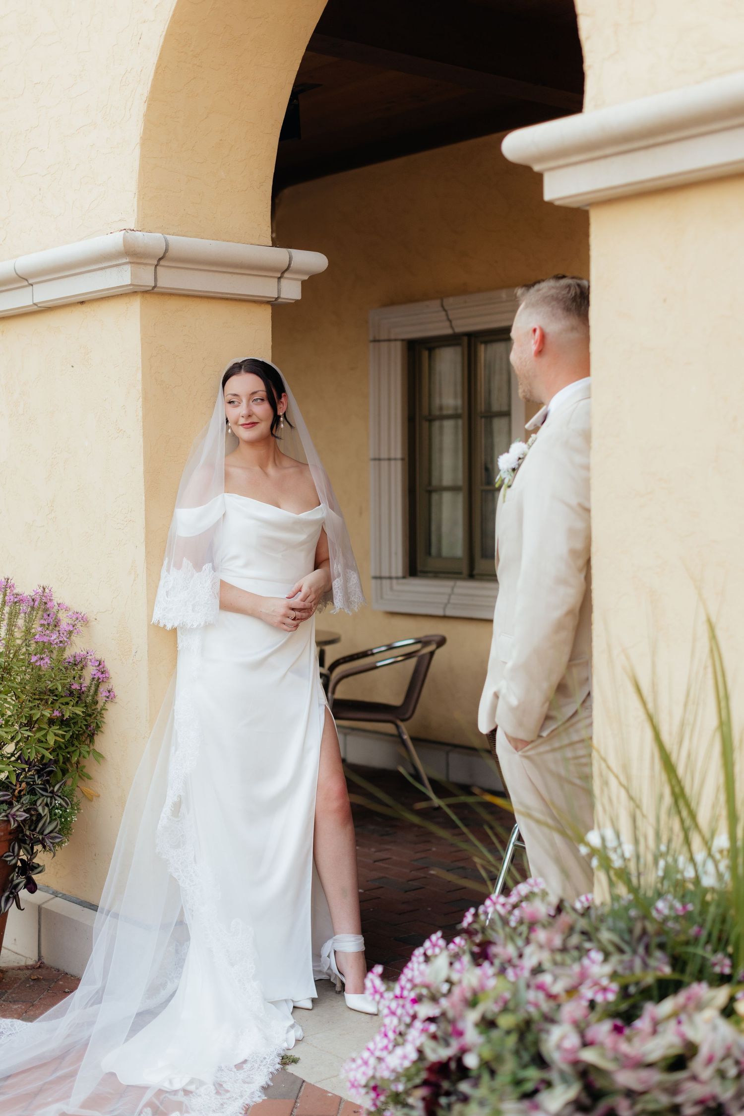 Wedding couple shares playful moment on outdoor patio with pink flowers in background.