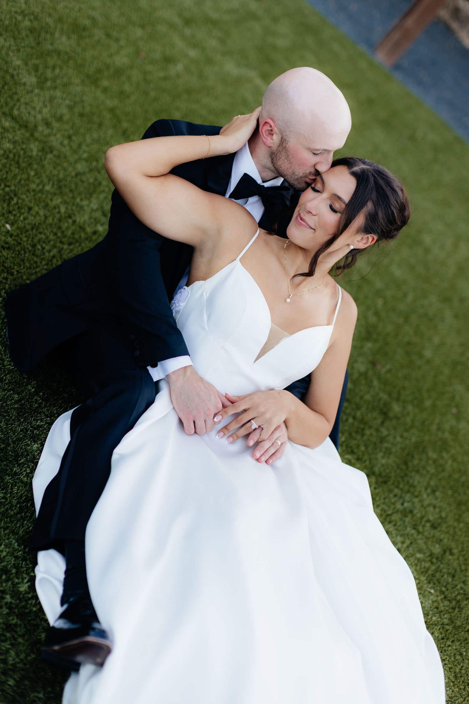 Bride and groom share intimate moments on green lawn during wedding photoshoot.