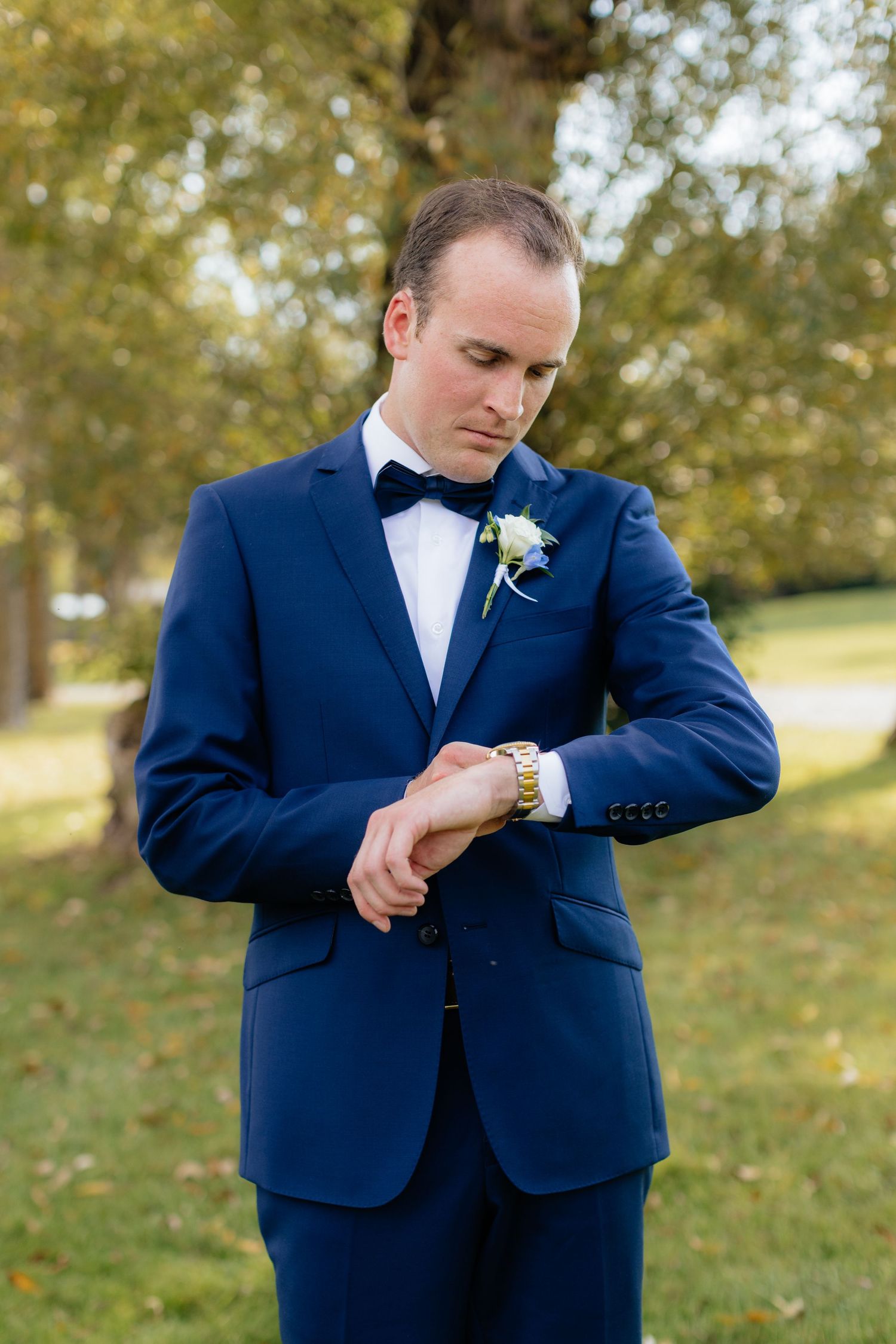 Groom in navy suit adjusts his cuffs during outdoor wedding portraits.