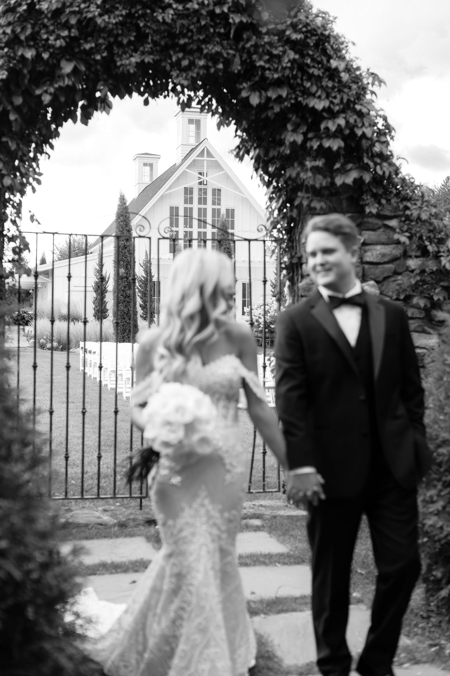Black and white wedding photo with couple walking through an ornate iron gate.