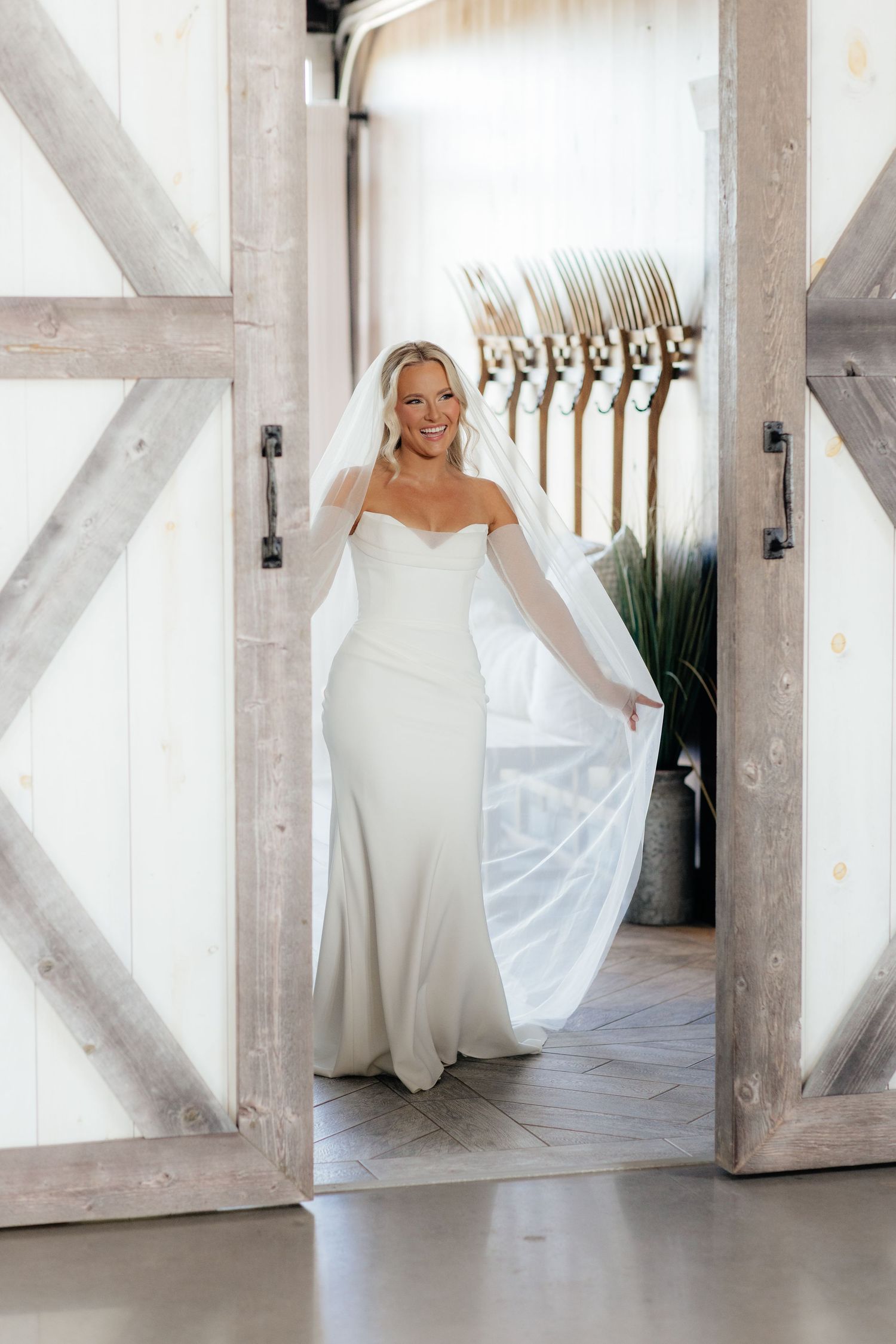 Bride in flowing white dress twirls through modern white barn venue.