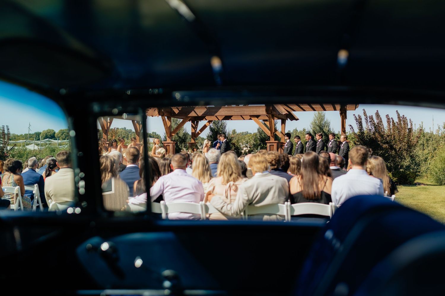 Panoramic view of outdoor wedding ceremony with guests seated under blue sky.