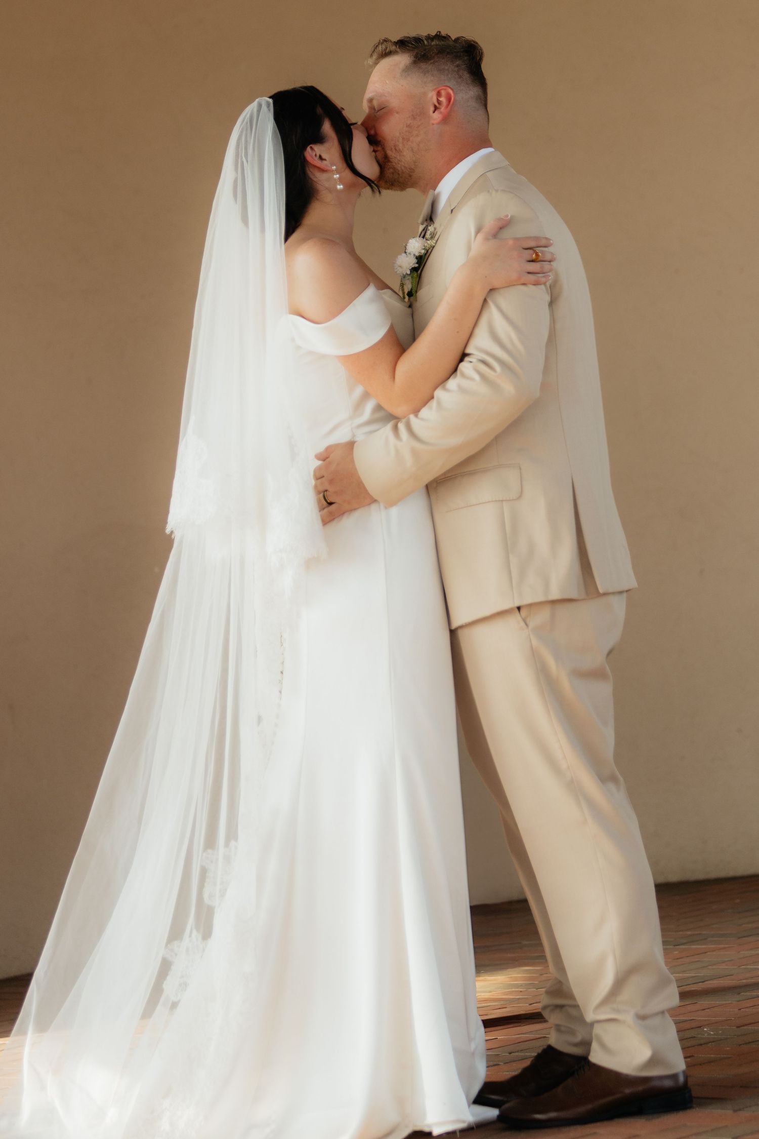 Romantic wedding couple shares intimate moments in formal attire against neutral backdrop.