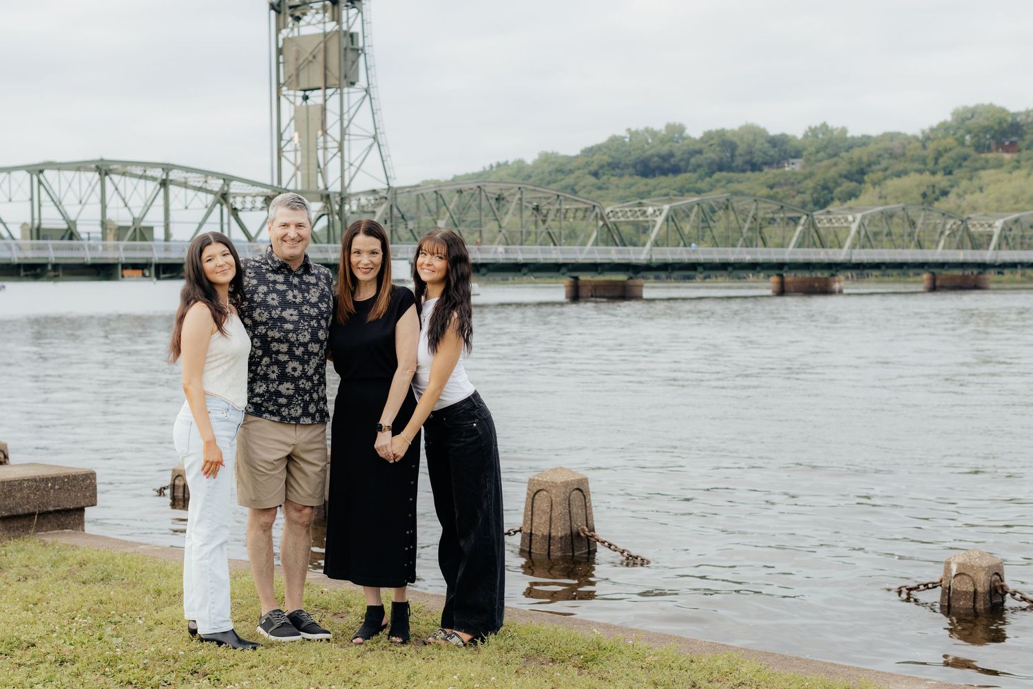 Family group poses together near a waterfront bridge on an overcast day.