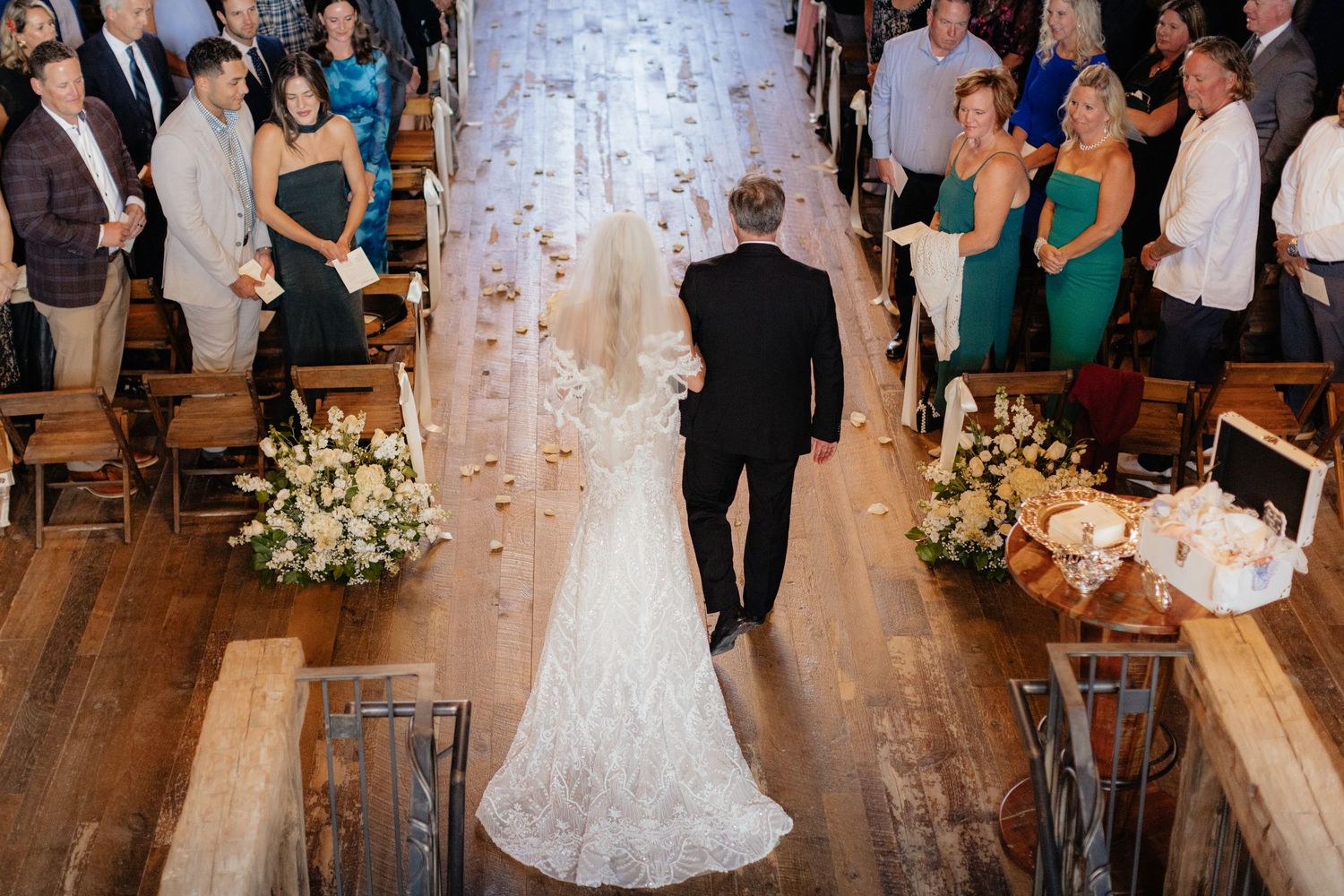 Wedding guests dance and celebrate on a rustic wooden dance floor under warm lighting.