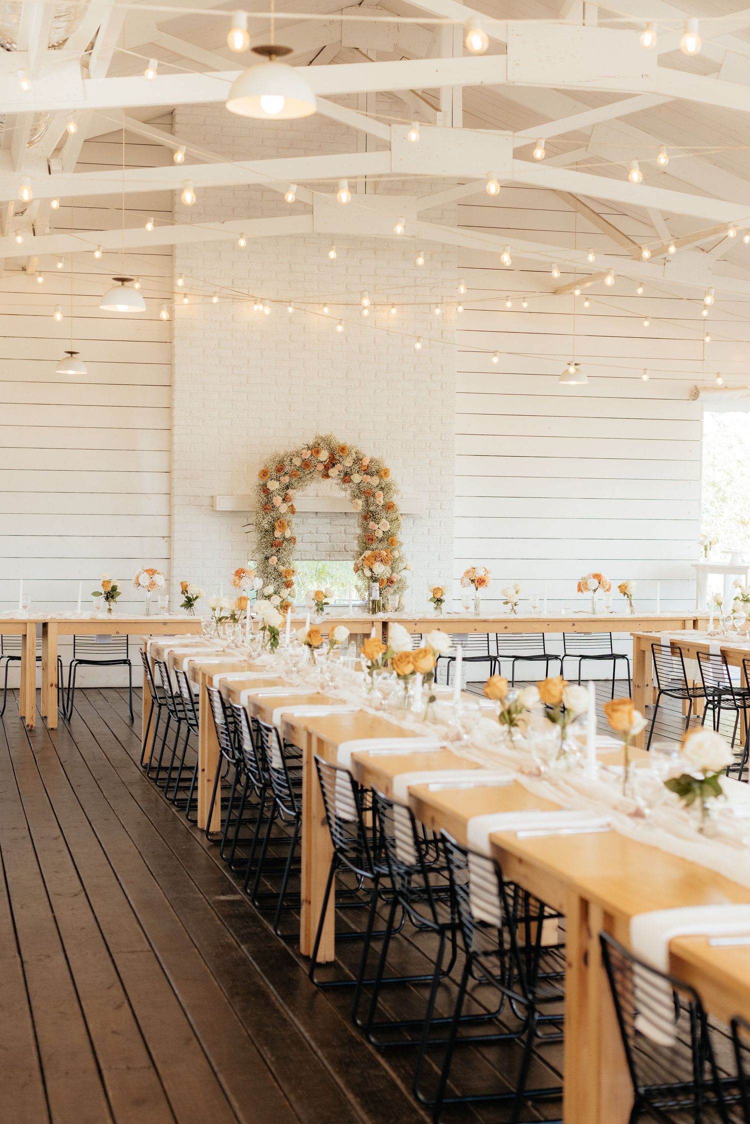 Reception venue with white walls, string lights, and long wooden tables set for dinner.