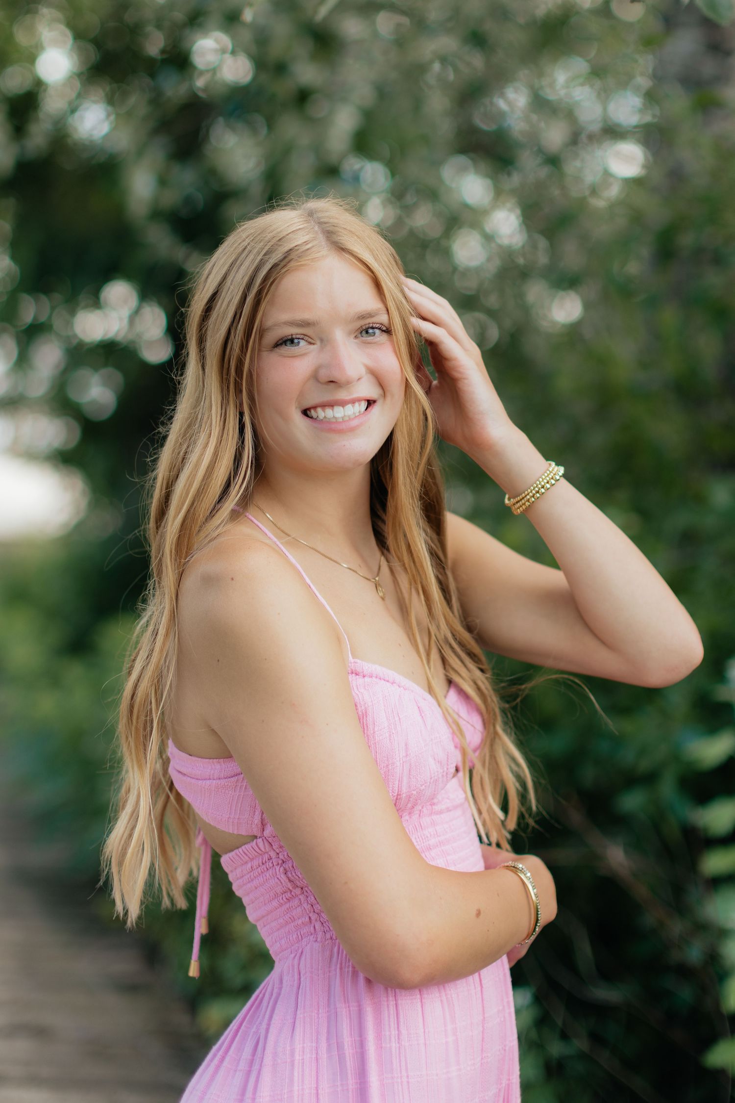 A pink summer dress is worn in a natural outdoor setting with greenery in the background.