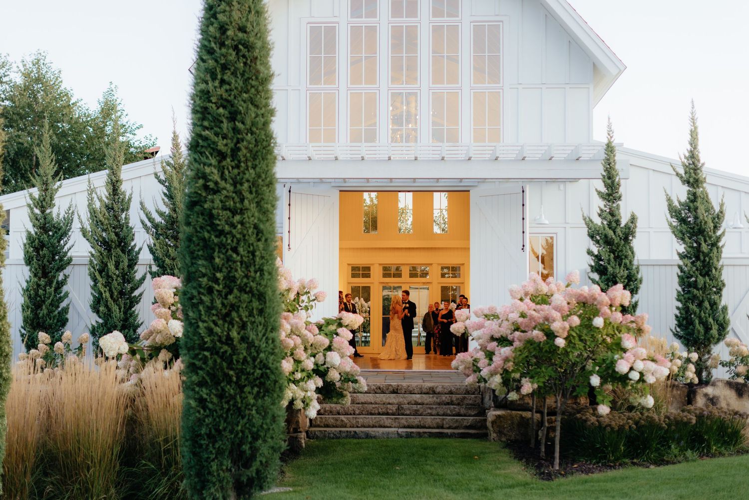 Modern white chapel venue exterior with cypress trees and landscaping at dusk.