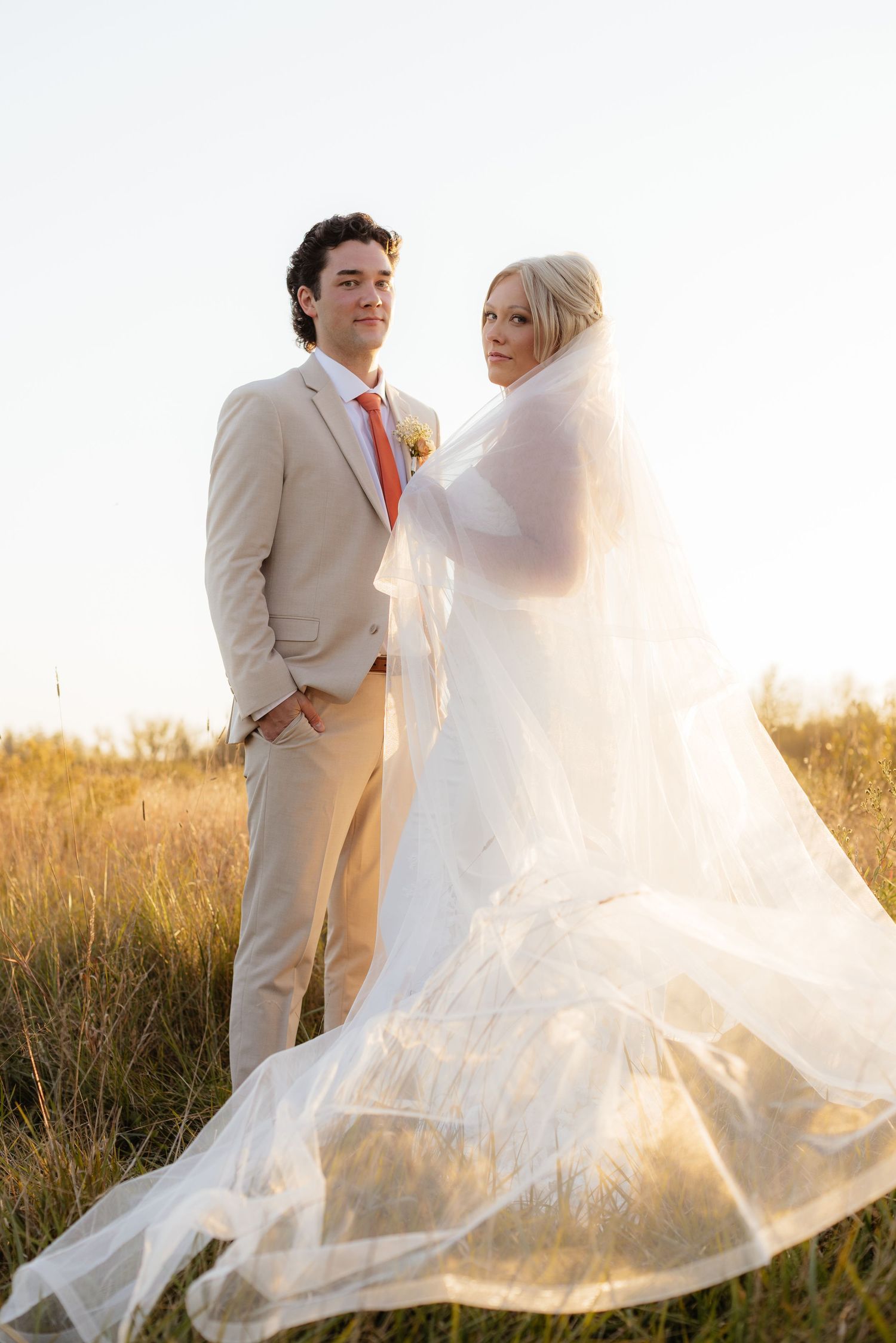 Wedding couple dancing in a field as bride's veil catches the sunset light.